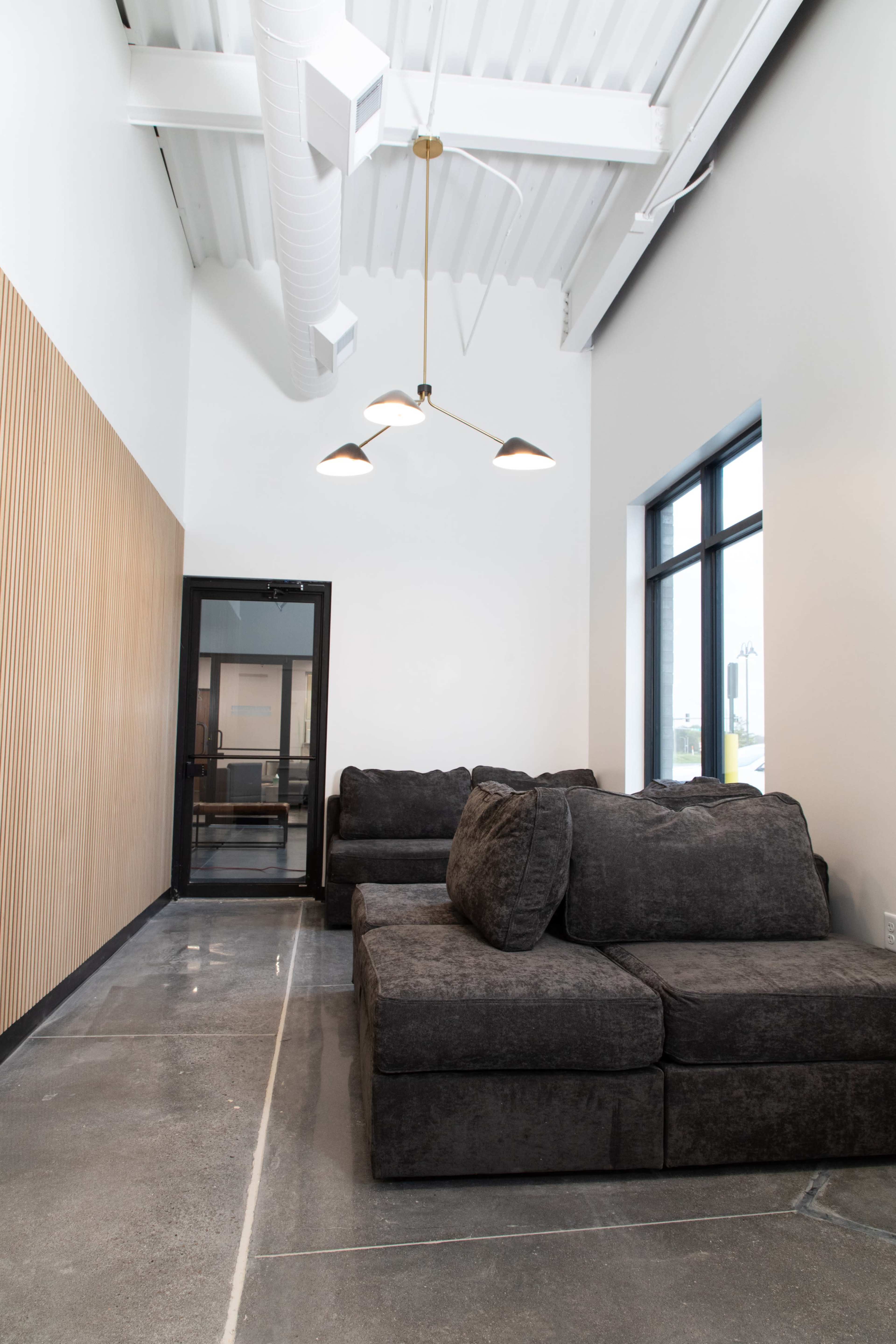 A modern lounge area featuring a dark gray sectional sofa, a large window, and a wooden accent wall.