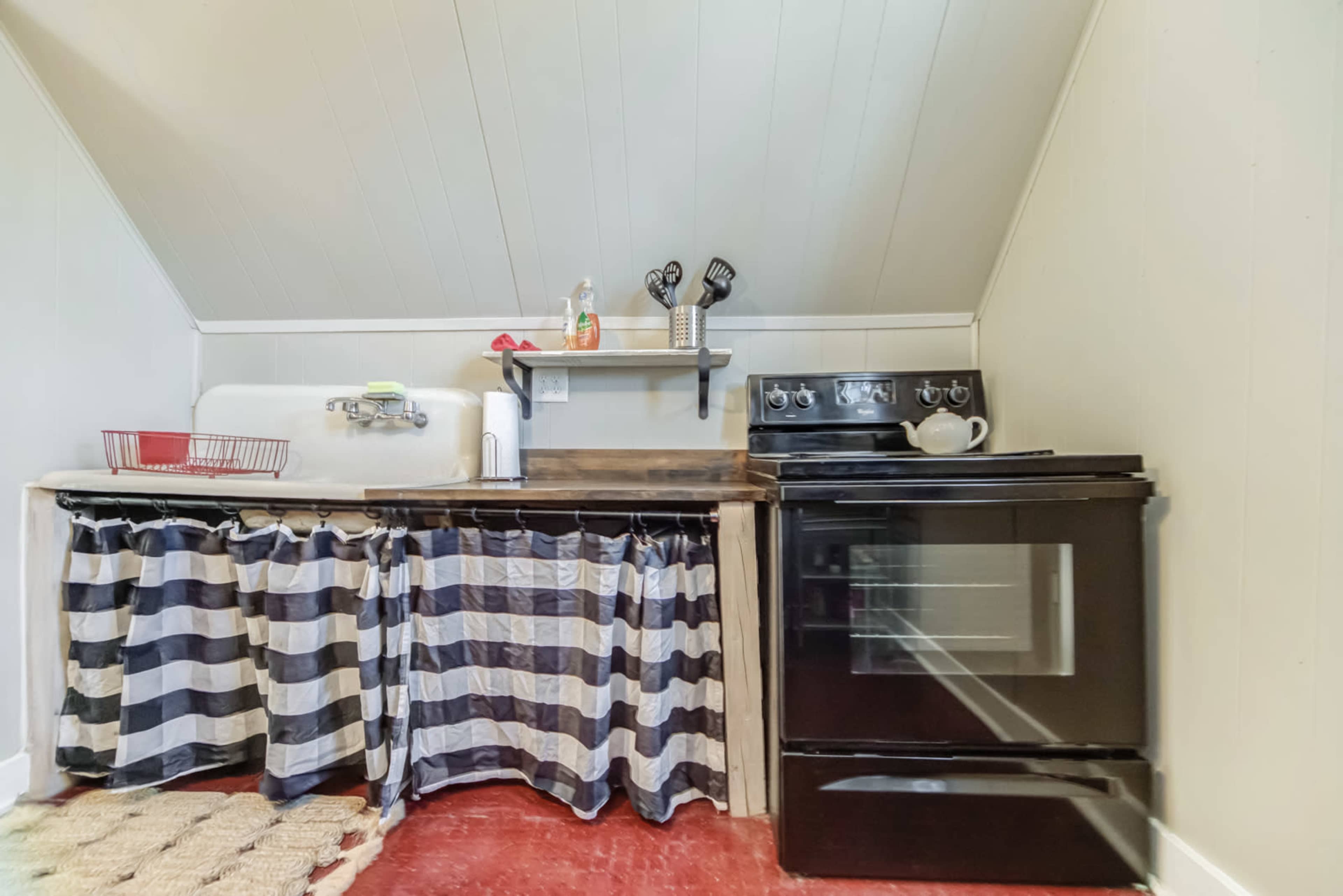 A compact kitchen with a black oven, a sink on the left, and striped curtains covering the space underneath the counter.