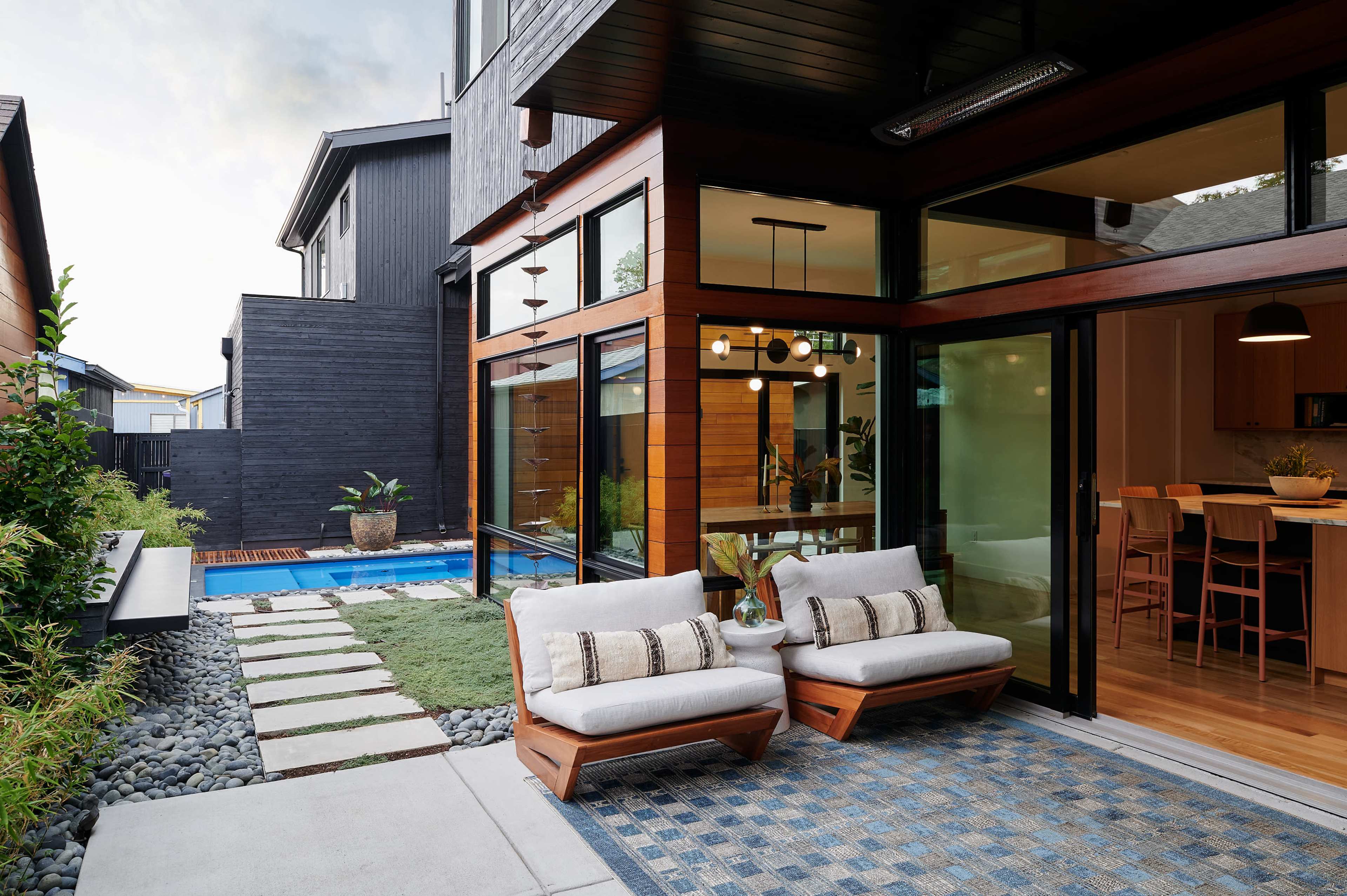 The image shows a modern backyard with two chairs facing a pool, surrounded by a landscaped area with stones and grassy patches.