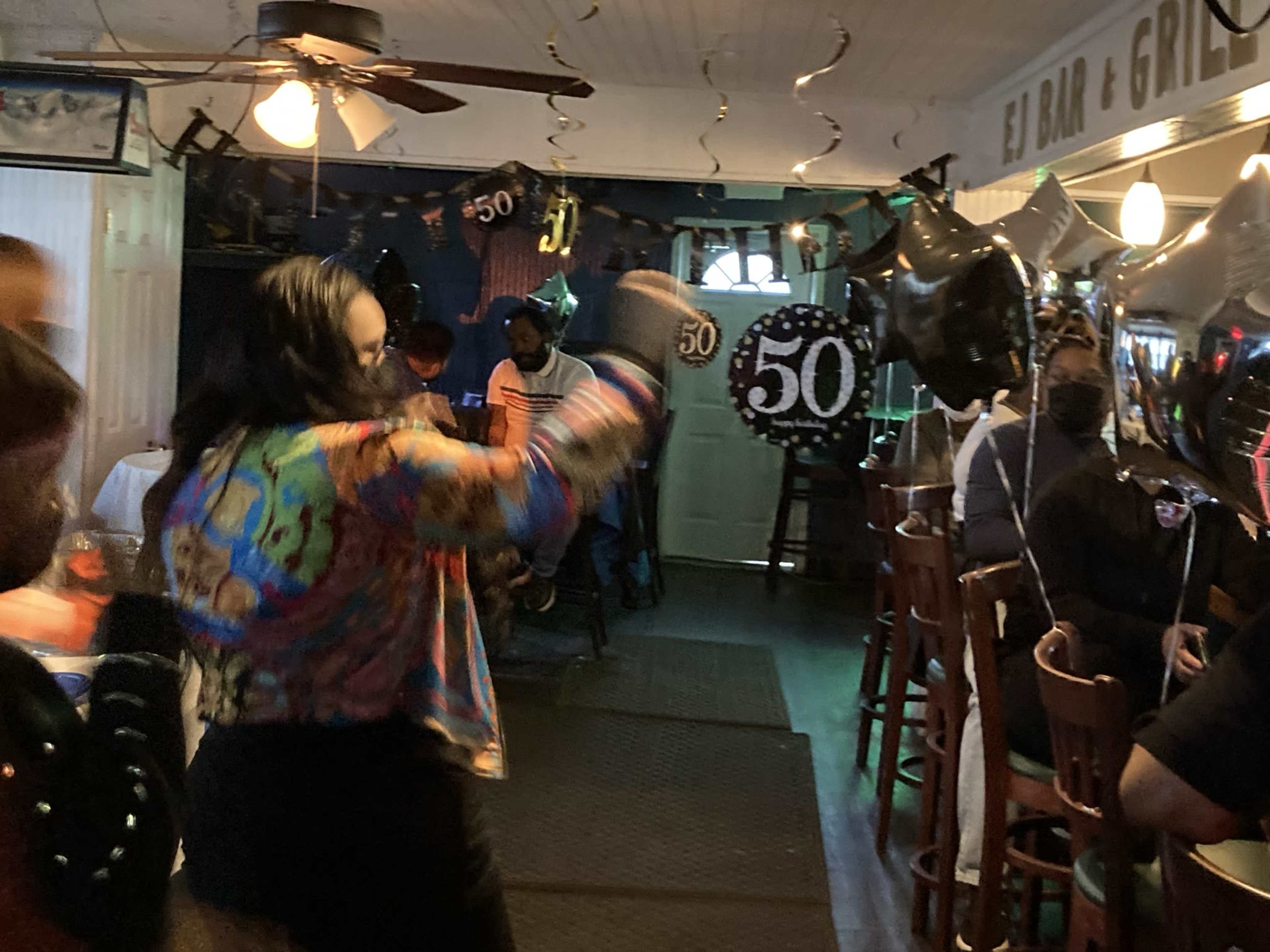 A woman in a colorful shirt dances at a bar decorated for a 50th birthday celebration.