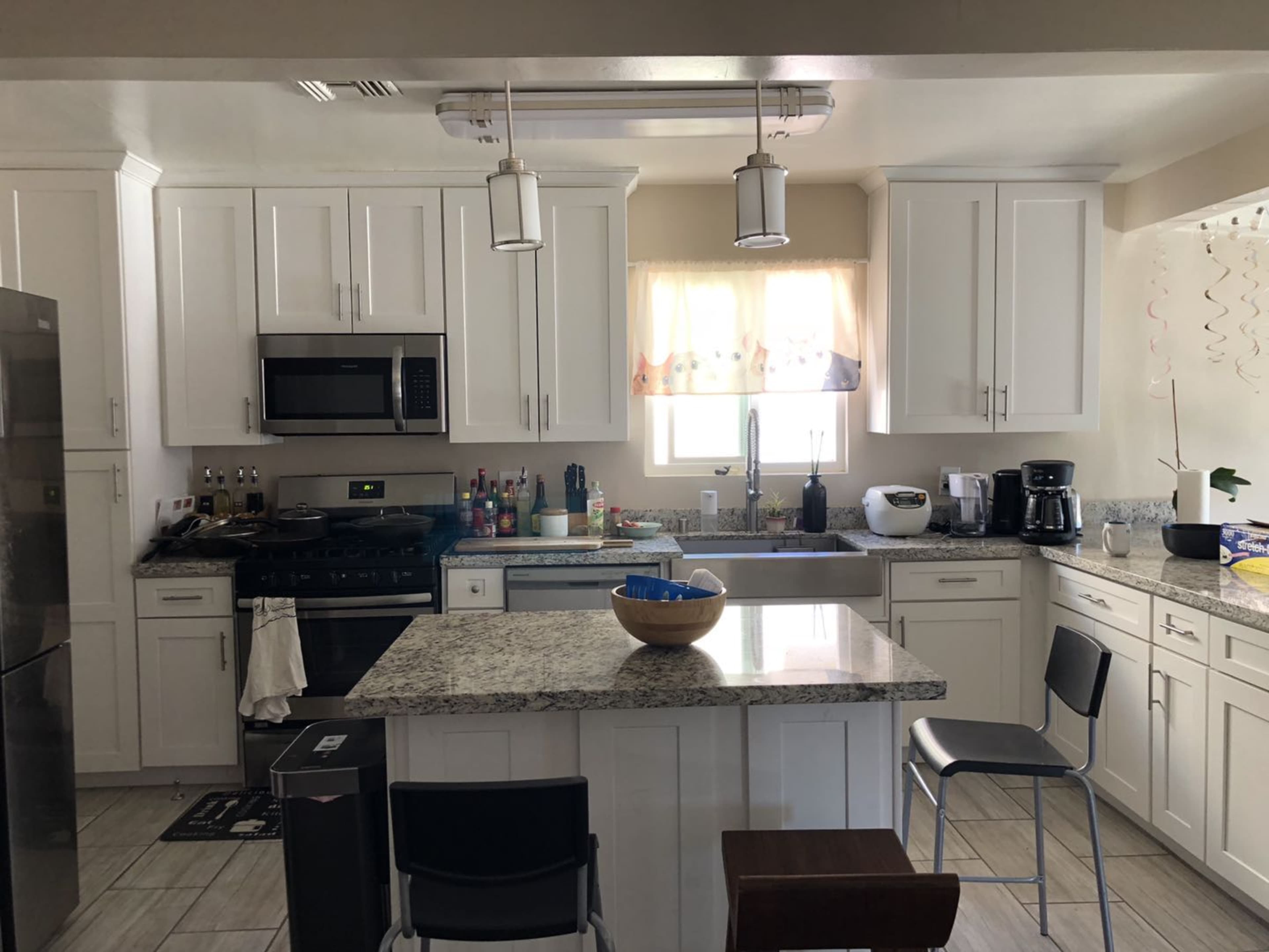 The image shows a modern kitchen with white cabinets, a granite countertop island, and stainless steel appliances.