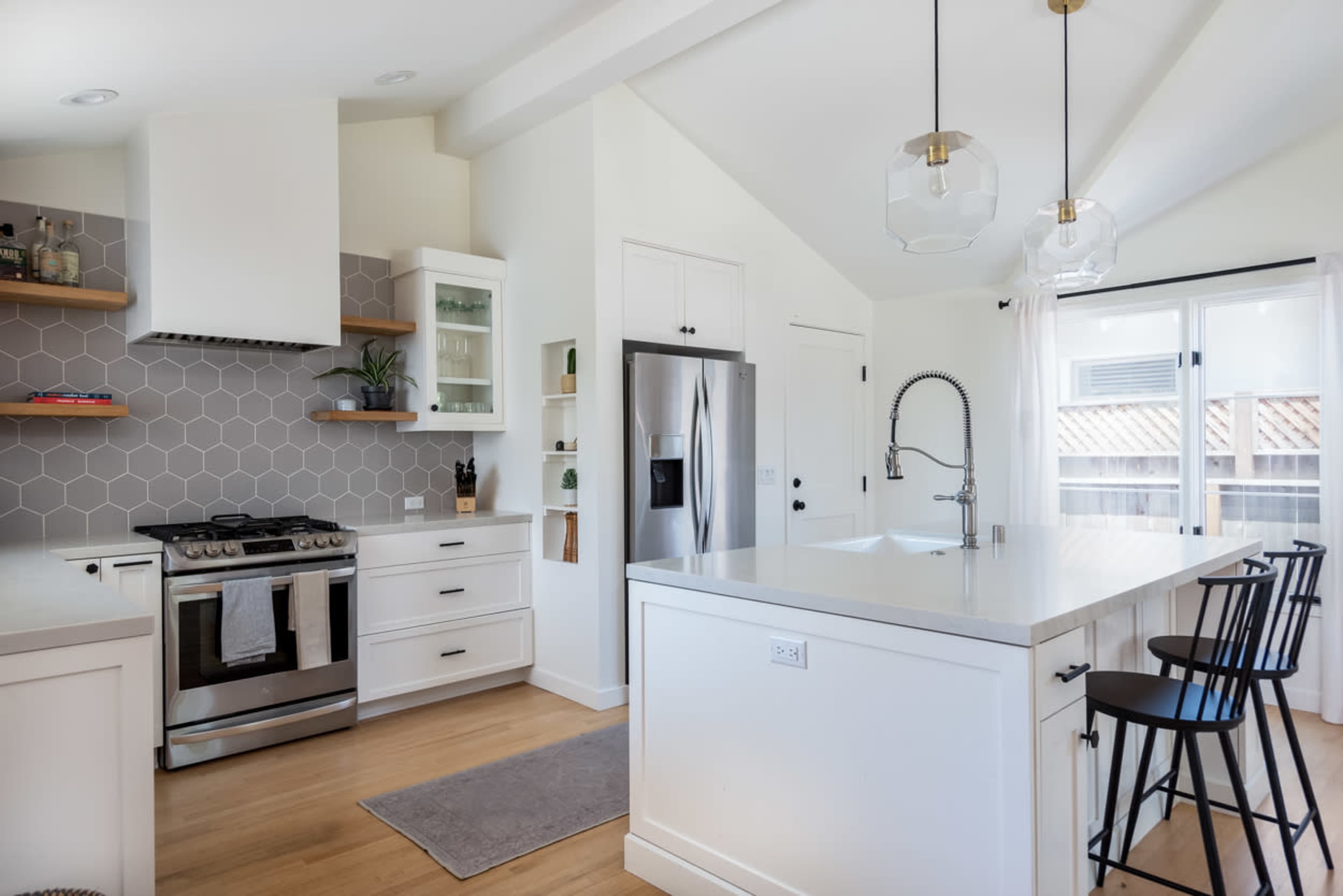 A modern kitchen featuring white cabinetry, a stainless steel refrigerator, a hexagonal tile backsplash, and a large island with bar stools.
