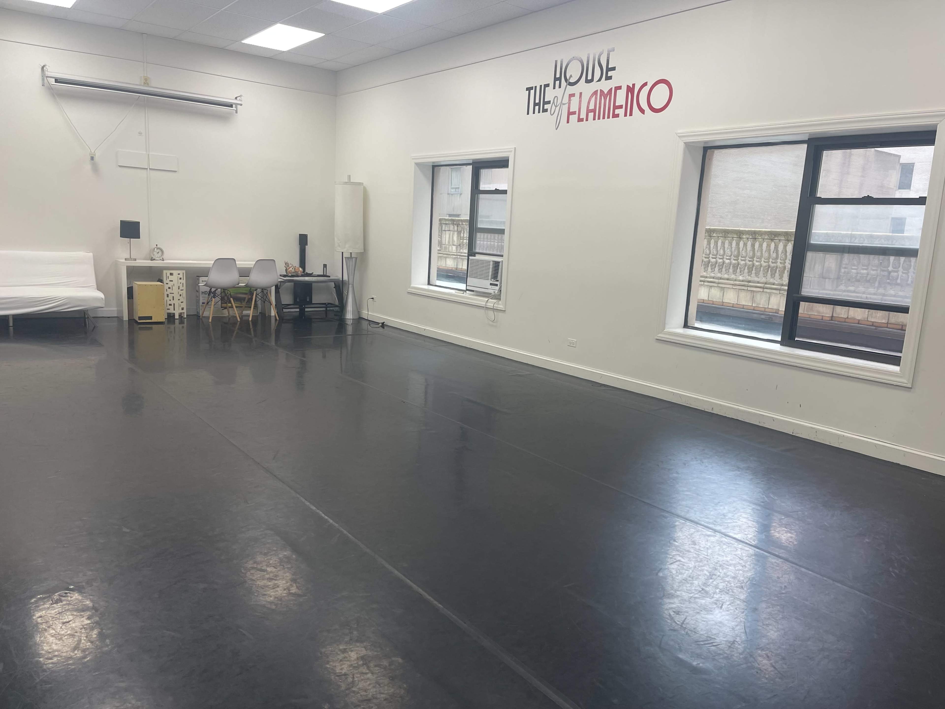 The image shows a spacious dance studio with a black floor, large windows, and the text "THE HOUSE OF FLAMENCO" on the wall.