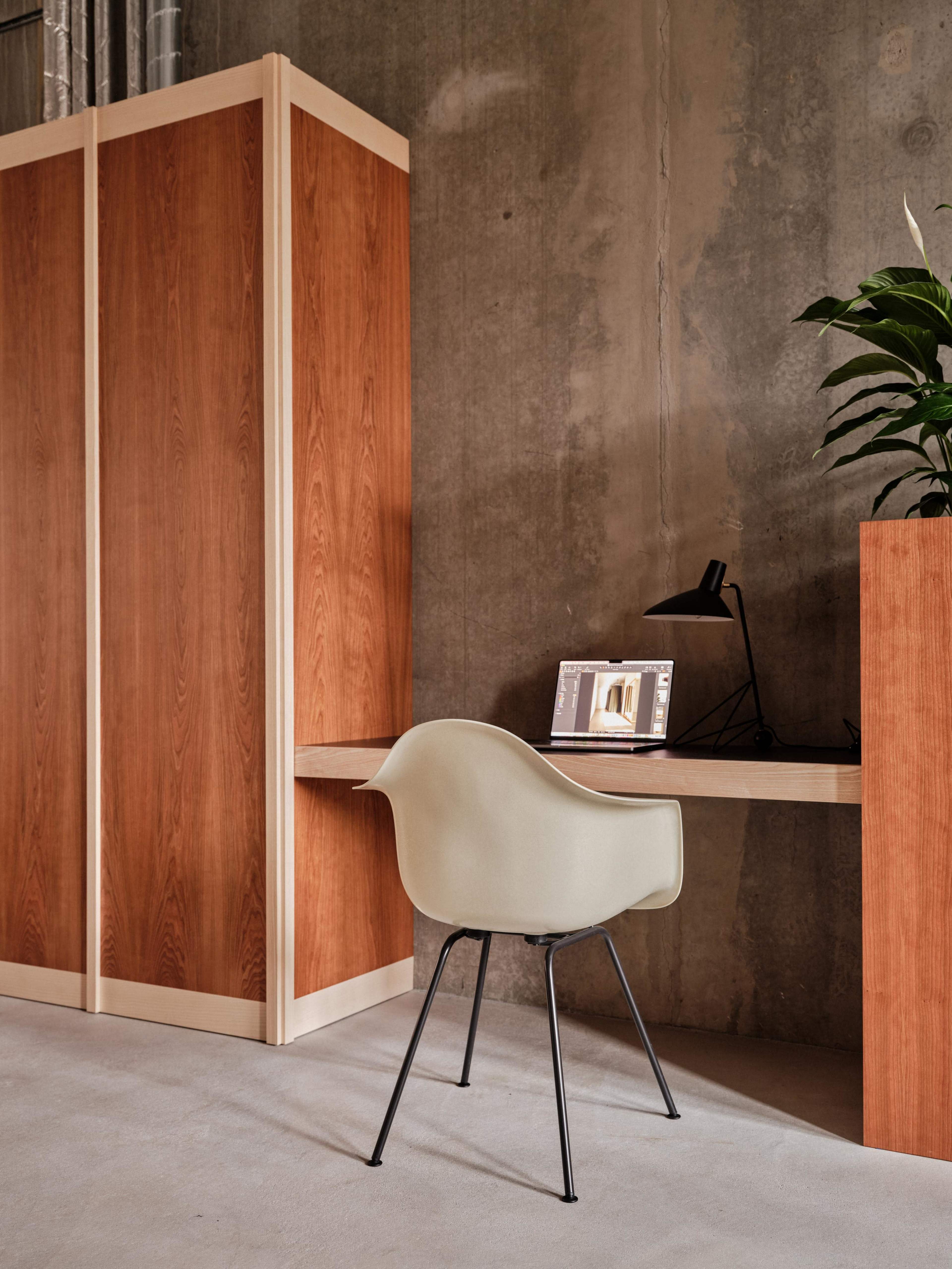 A minimalistic workspace with a chair at a wooden desk, backed by a wooden divider and adorned with a potted plant.
