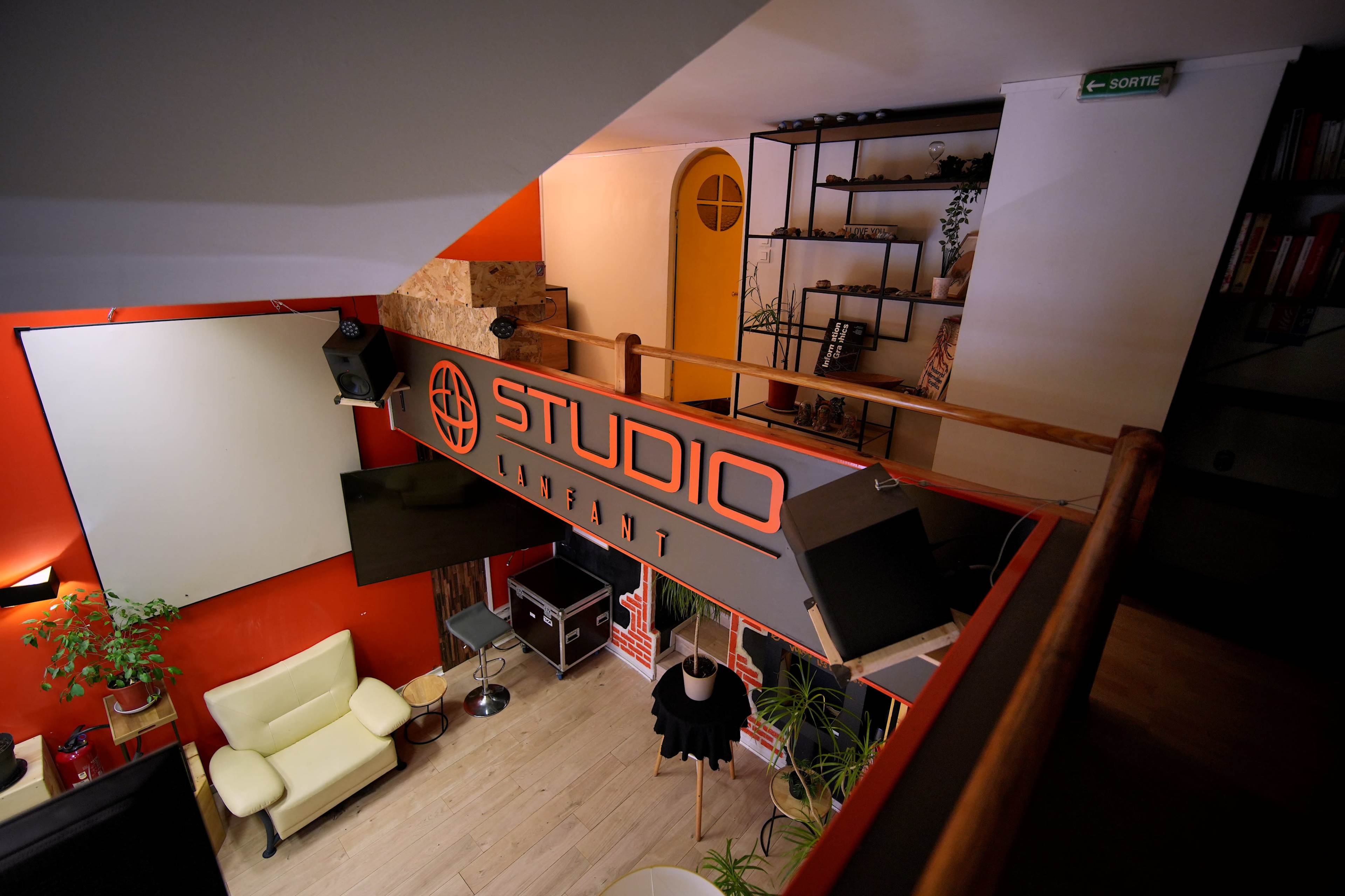 The image shows a brightly lit studio space featuring a large "STUDIO INSTANT" sign, a green plant, a yellow armchair, and various decorative shelves.