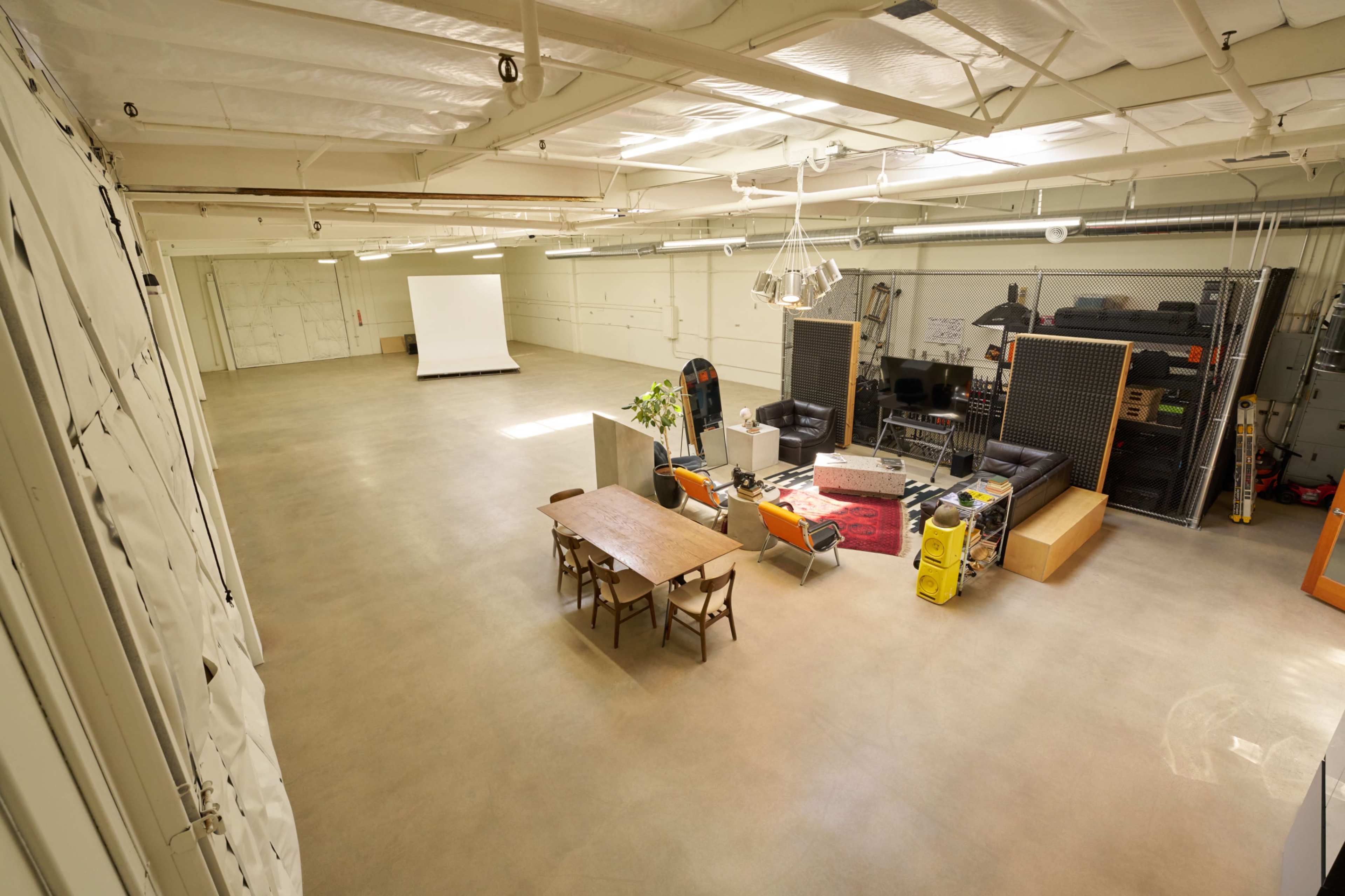 The image shows a spacious, empty studio with a table, chairs, and various equipment placed around, including a projection screen at one end.