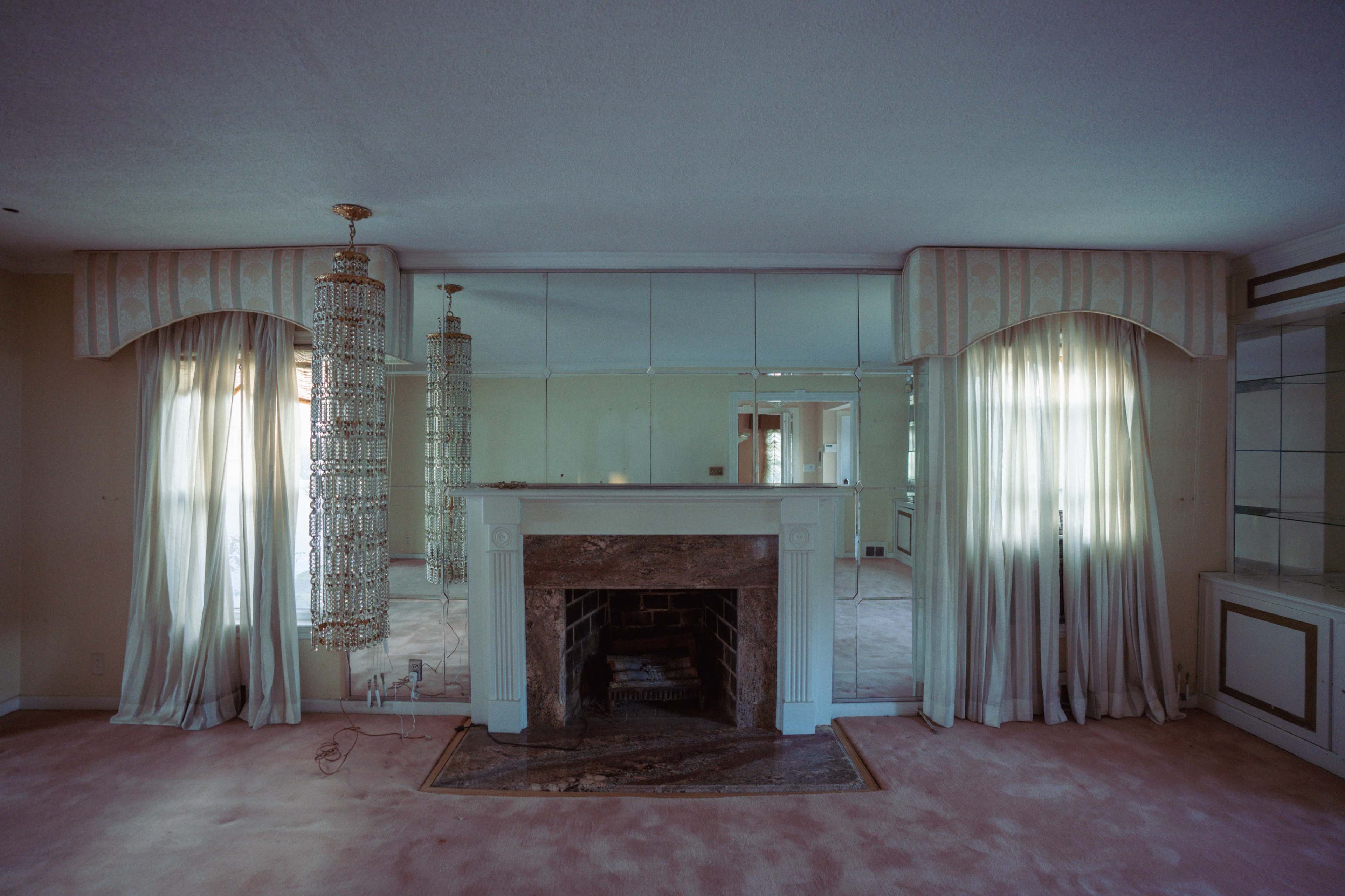 The image shows a living room with a mirrored wall, a fireplace with a marble mantel, and two hanging crystal chandeliers.
