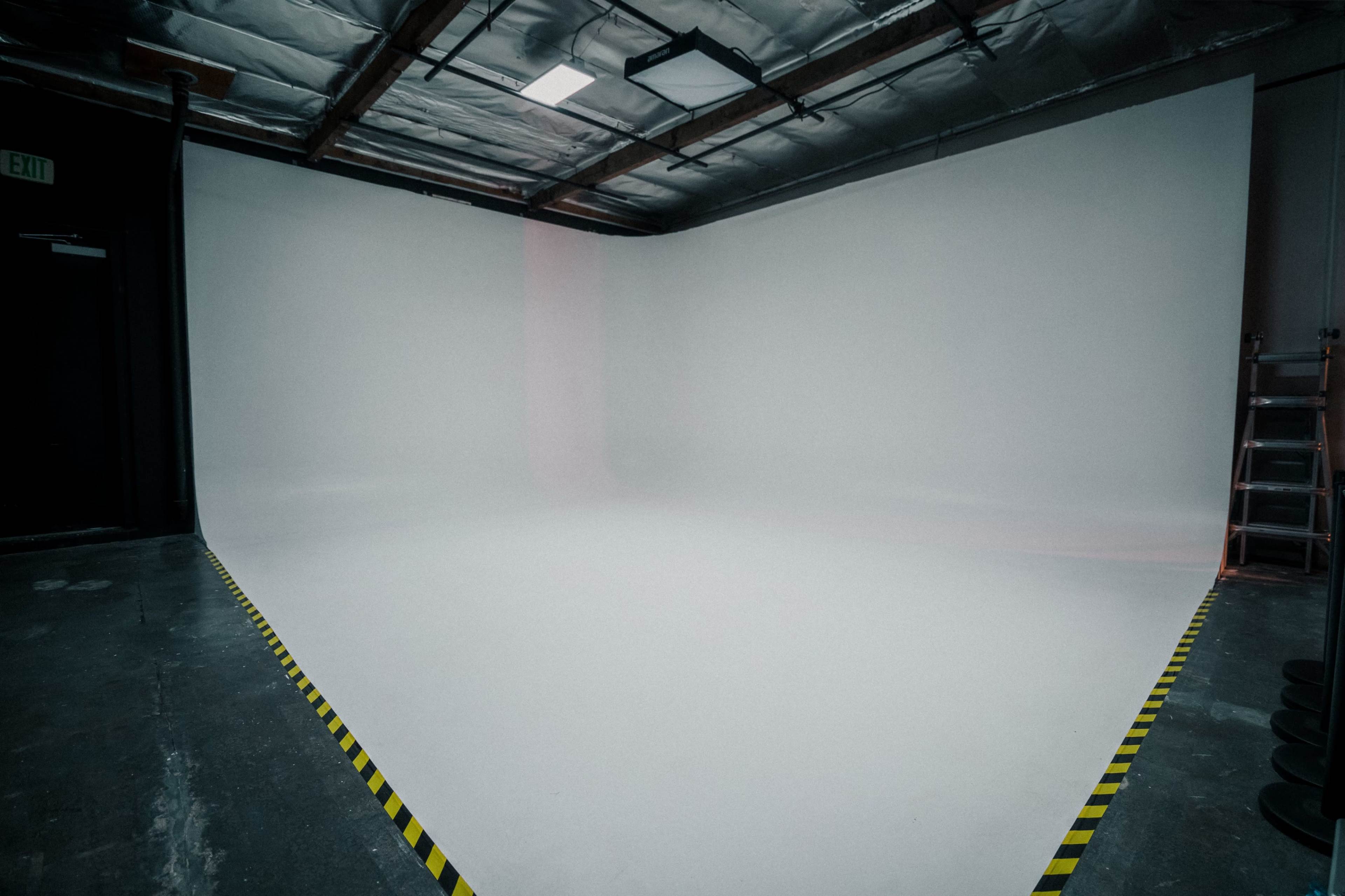 An empty photo studio with a large white backdrop and black and yellow caution tape along the floor.