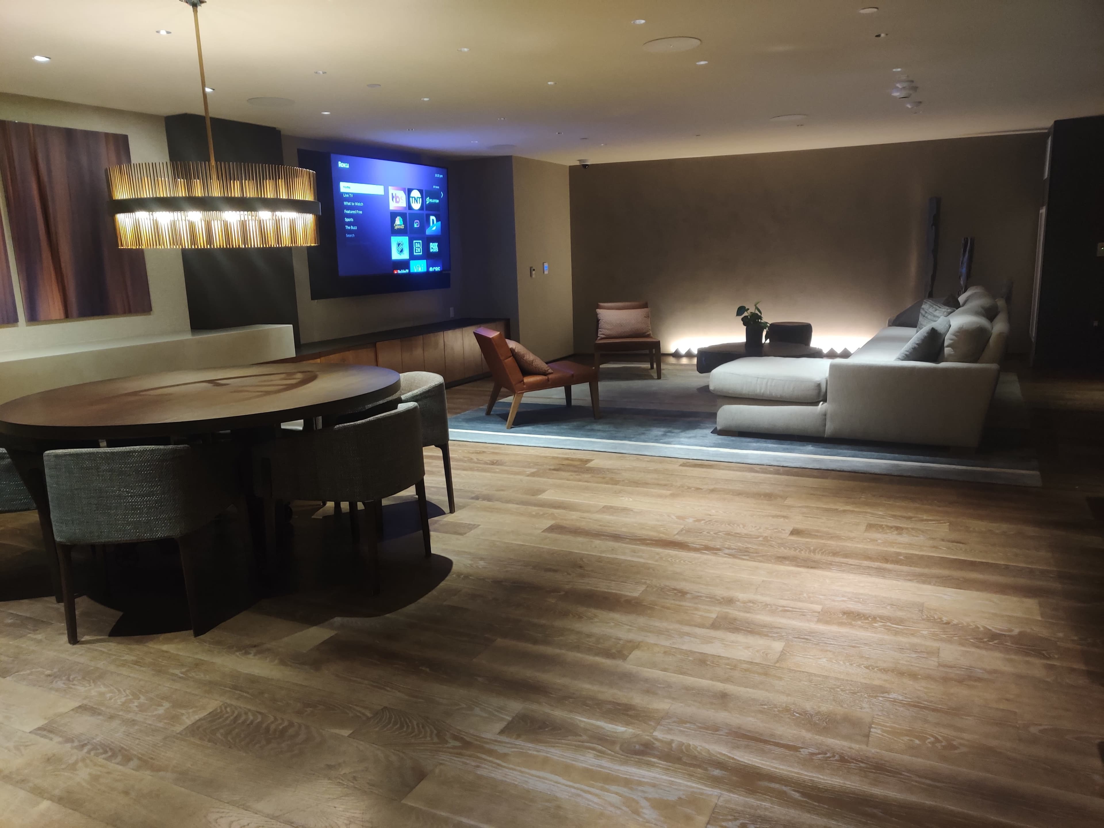 A modern living space with a circular dining table, a large sectional sofa, an armchair, and a wall-mounted TV.