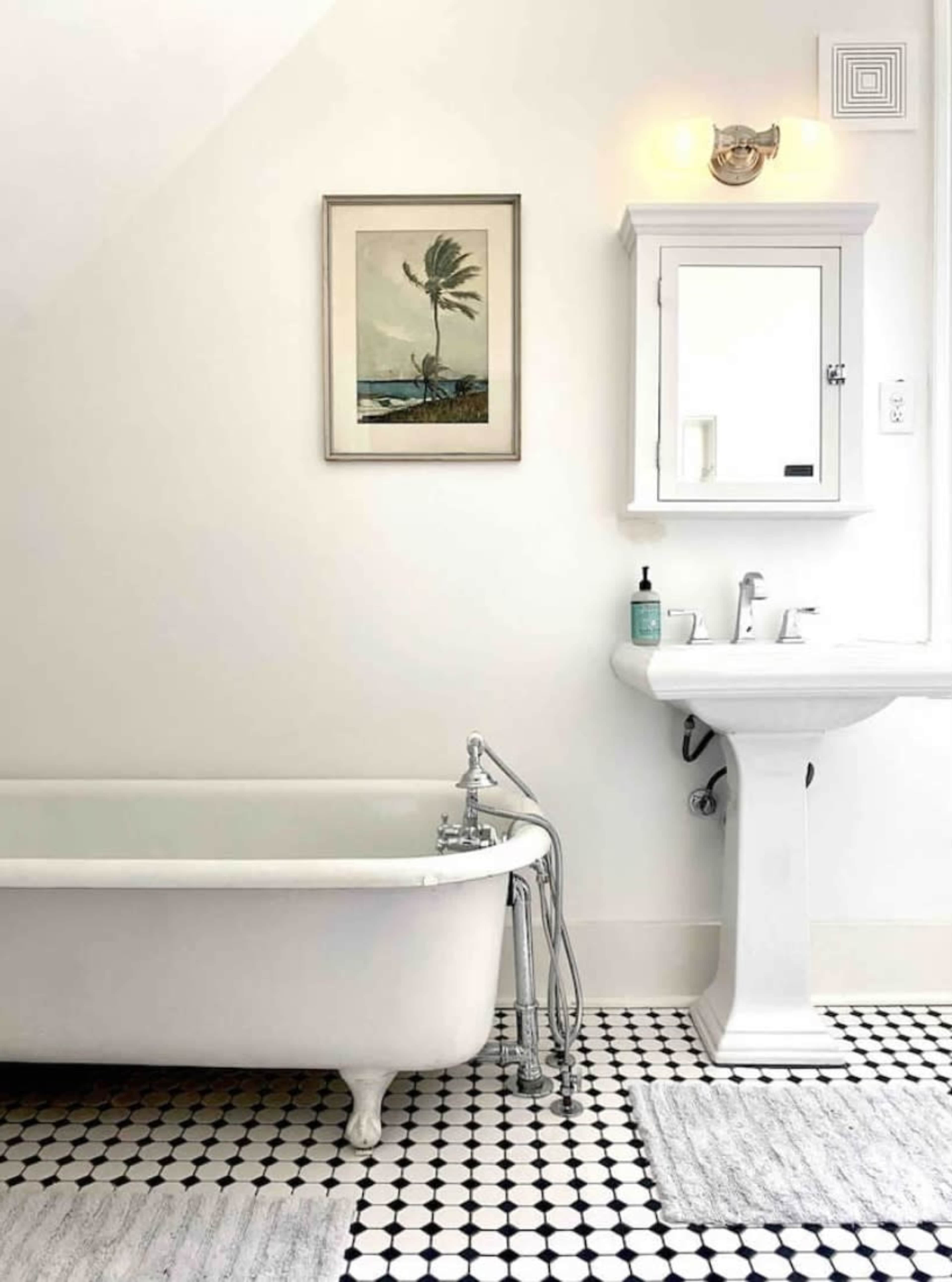 The image shows a bathroom with a freestanding white bathtub, a pedestal sink, and a wall-mounted mirror, all set against a backdrop of white walls and black and white tiled floor.