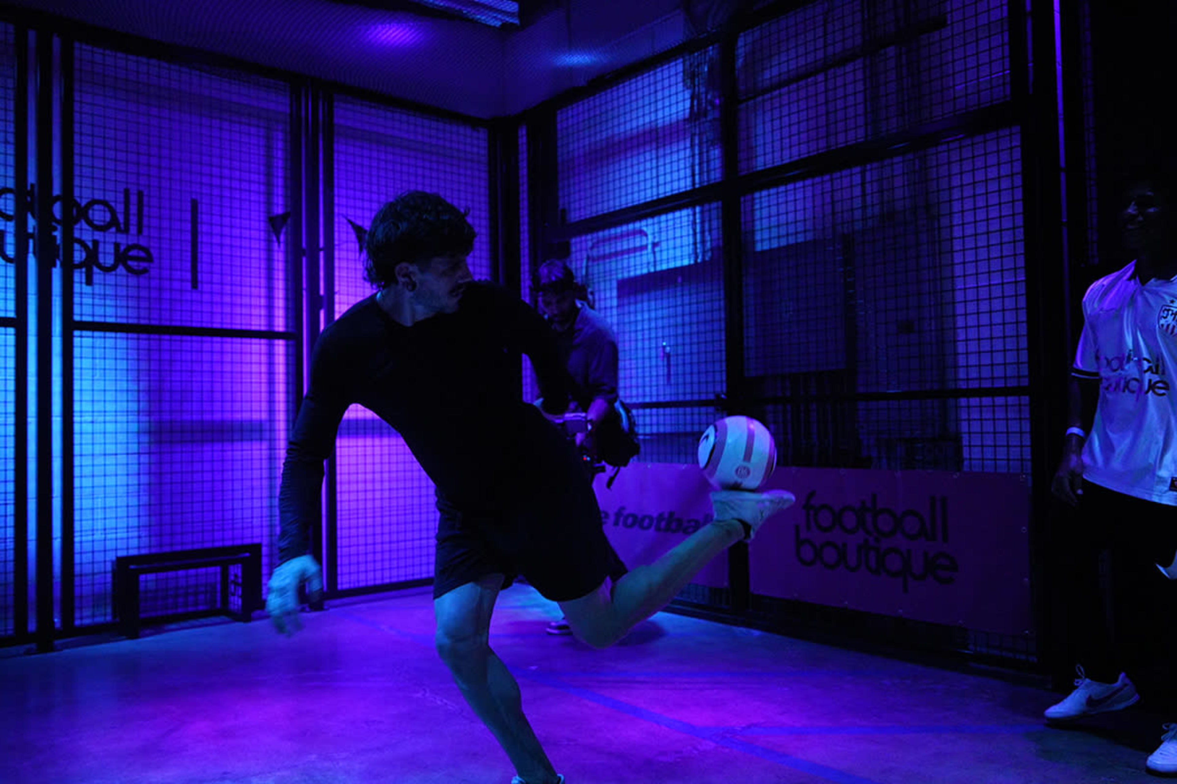 A player kicks a soccer ball in a dimly lit room with purple lighting and a grid-like backdrop.