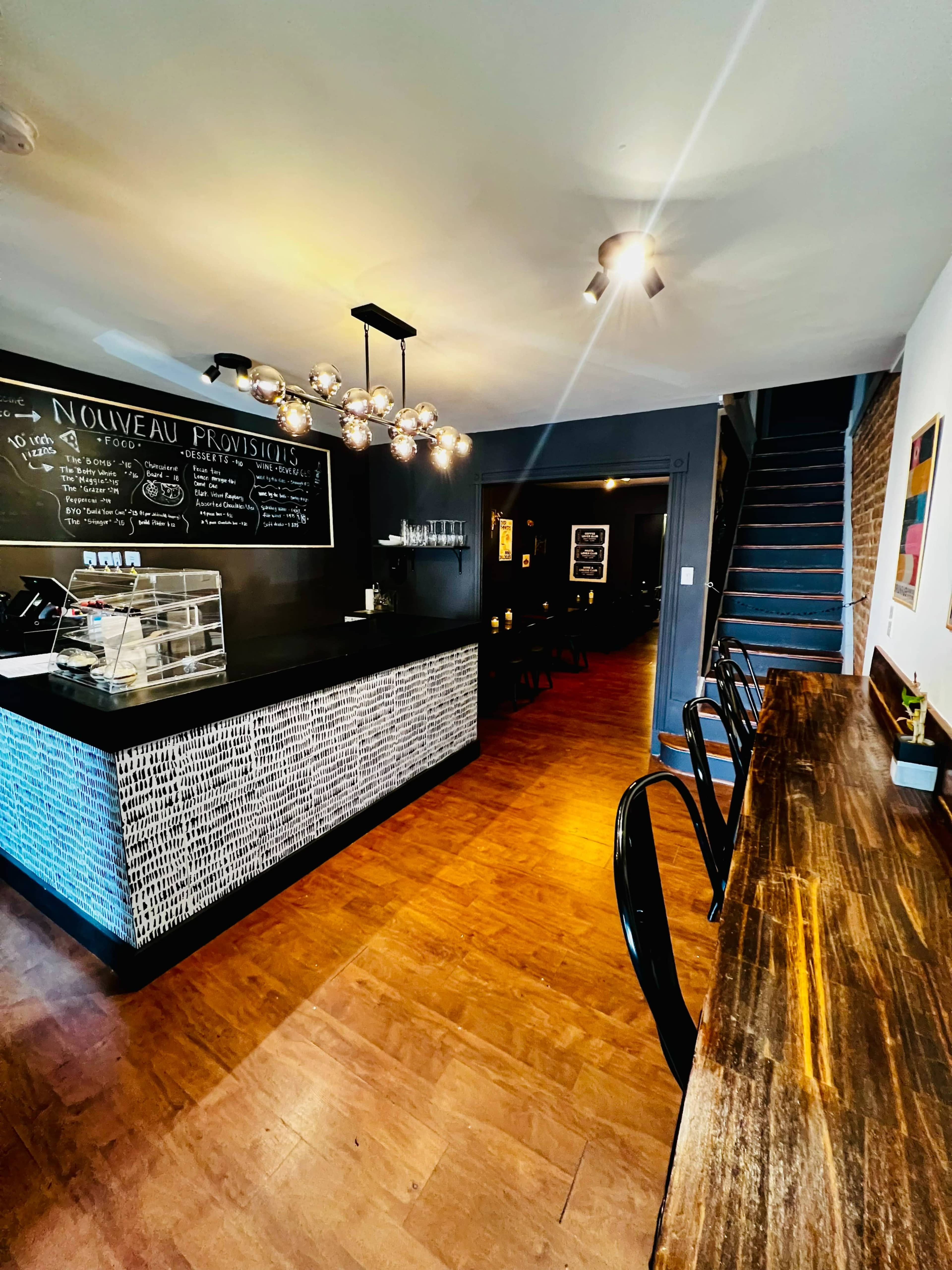 The image shows a modern café interior with a black counter, wooden tables, and a staircase leading to an upper level.