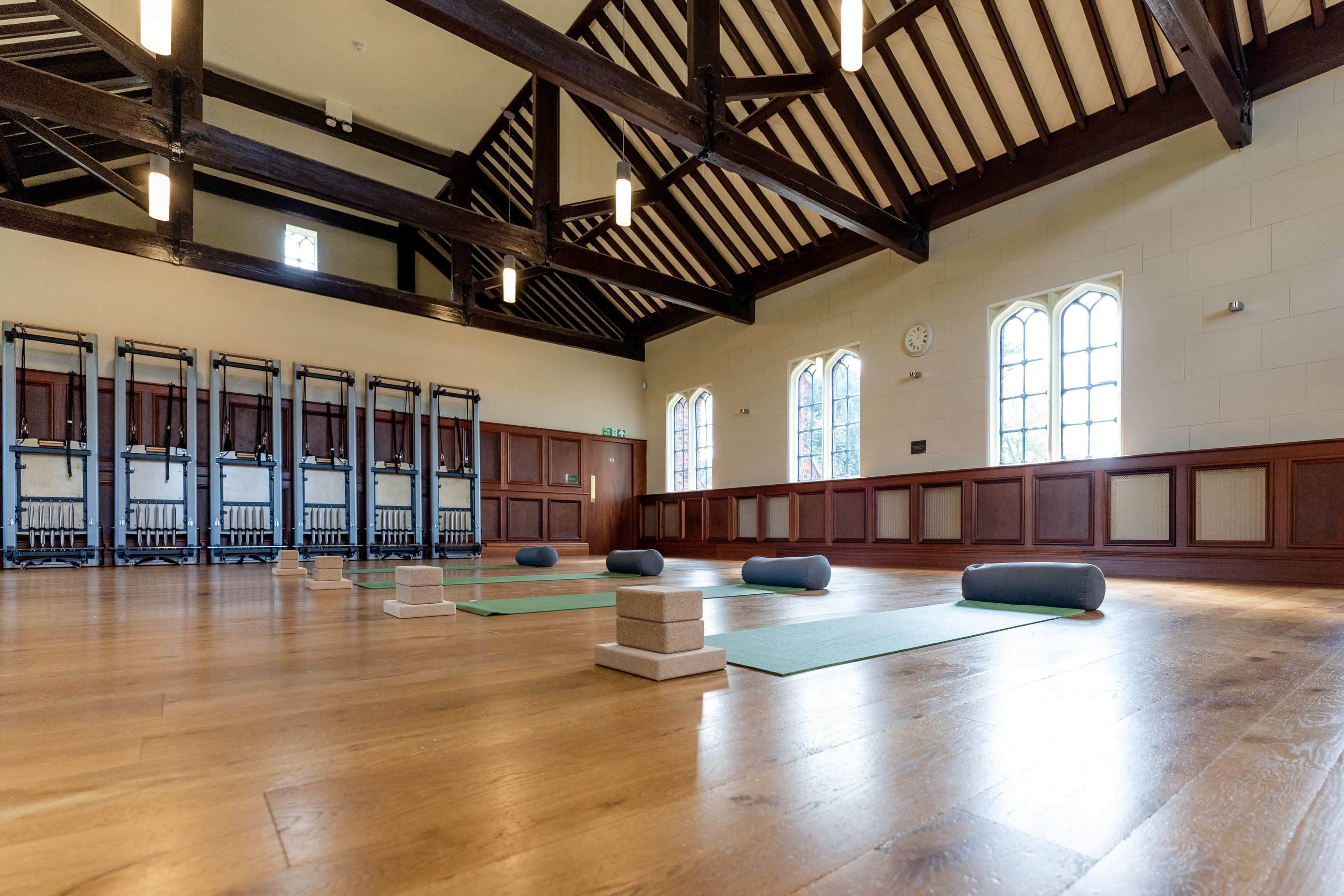A spacious yoga studio with wooden beams, several yoga mats placed on the wooden floor, and exercise blocks positioned on the mats.