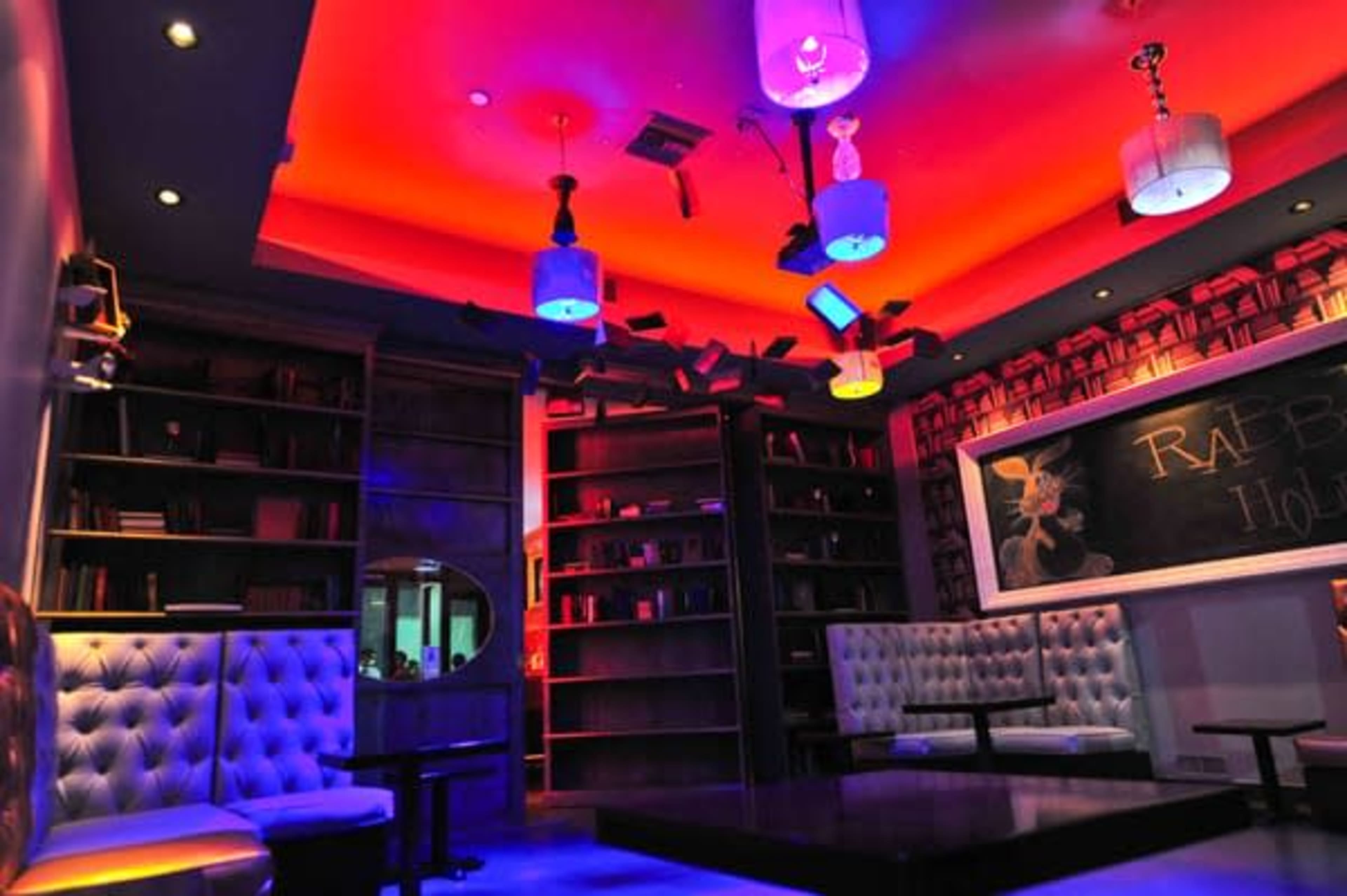 A colorful, modern lounge with bookshelves, plush seating, and dramatic overhead lighting.