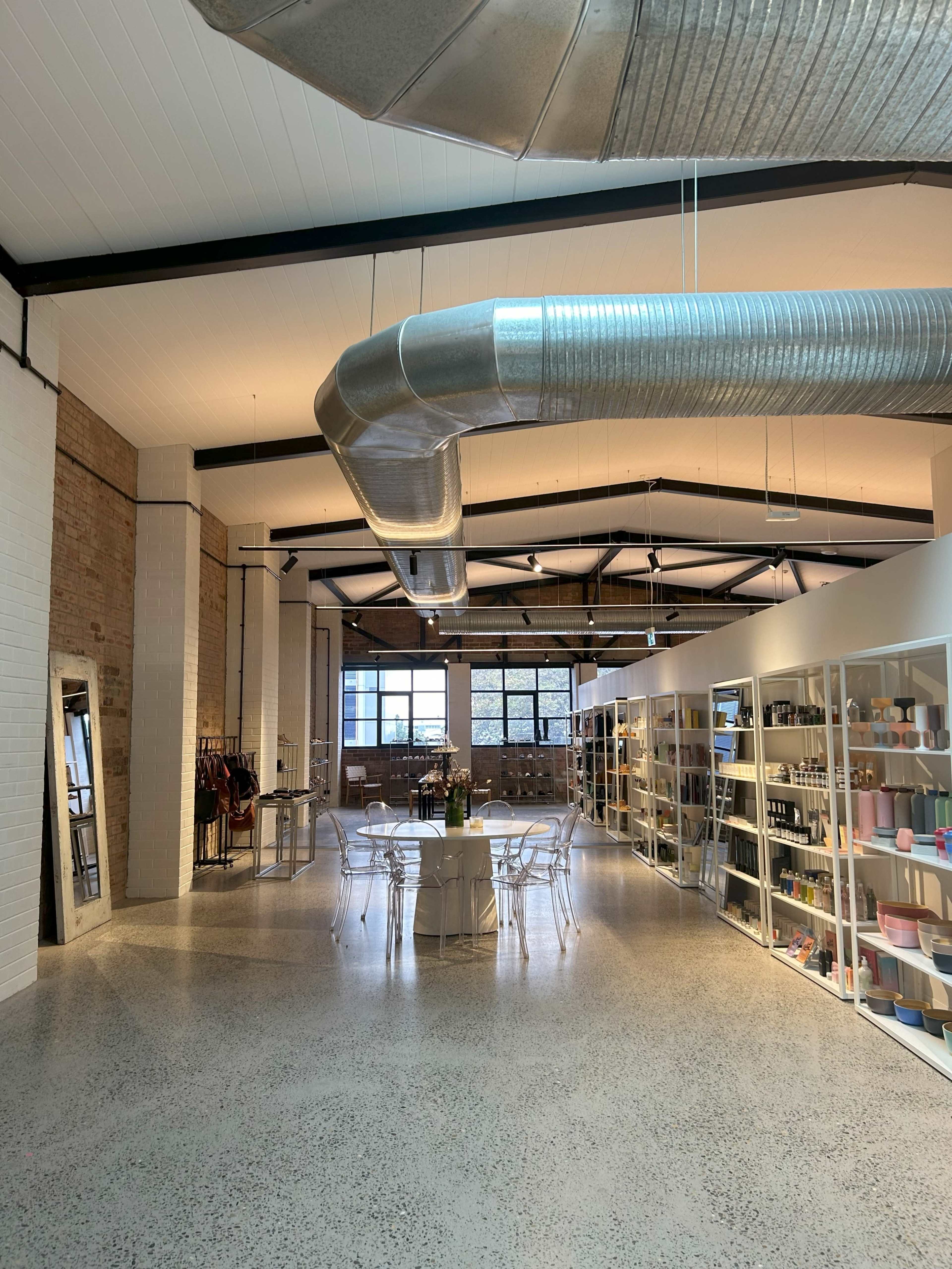 A spacious interior with a dining area featuring white furniture and a well-organized display of various products along the walls.