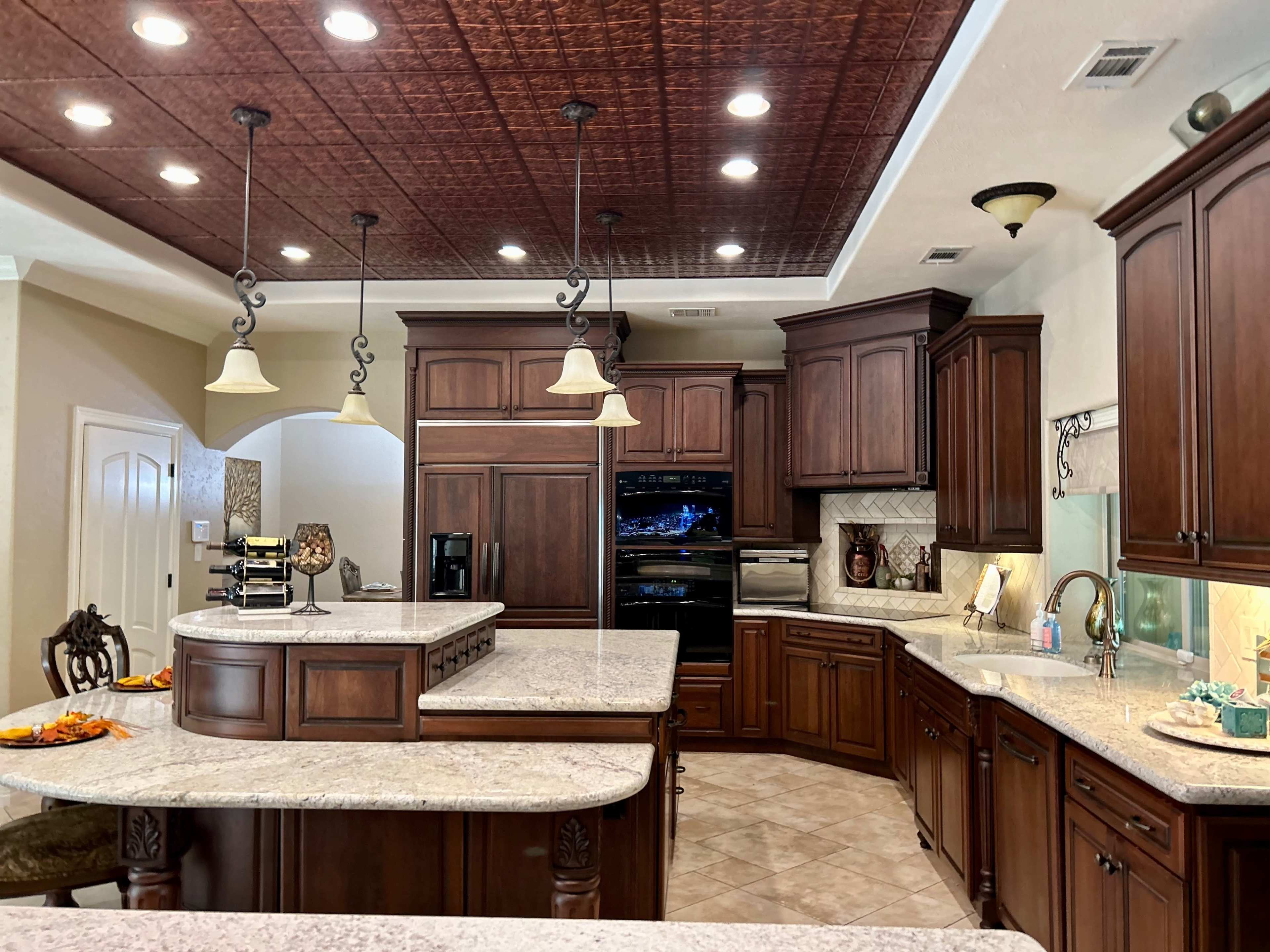 A spacious kitchen with dark wooden cabinetry, granite countertops, and modern appliances, featuring an island with seating and pendant lights.