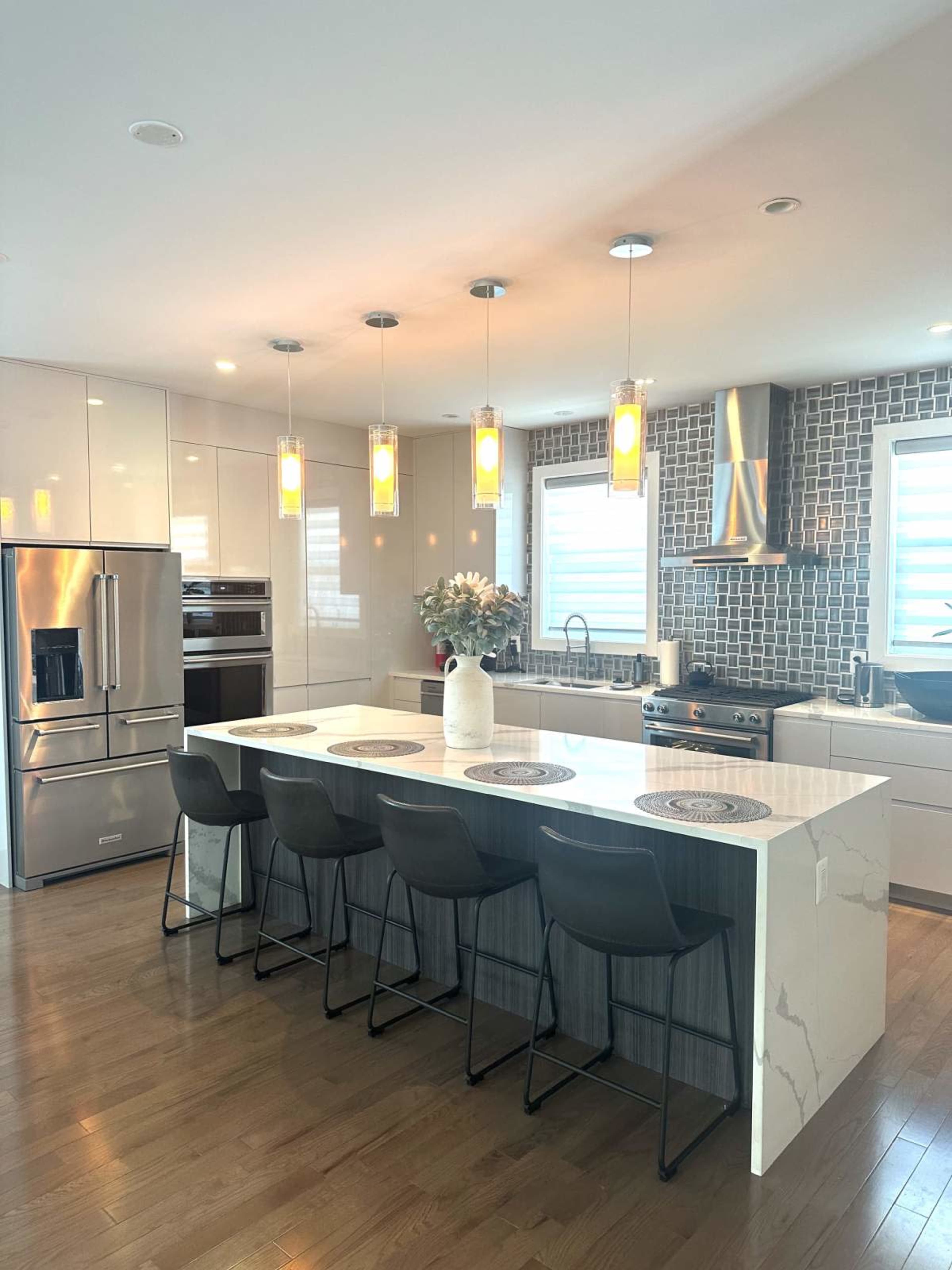 A modern kitchen features a large island with bar seating, stainless steel appliances, and pendant lights illuminating the space.