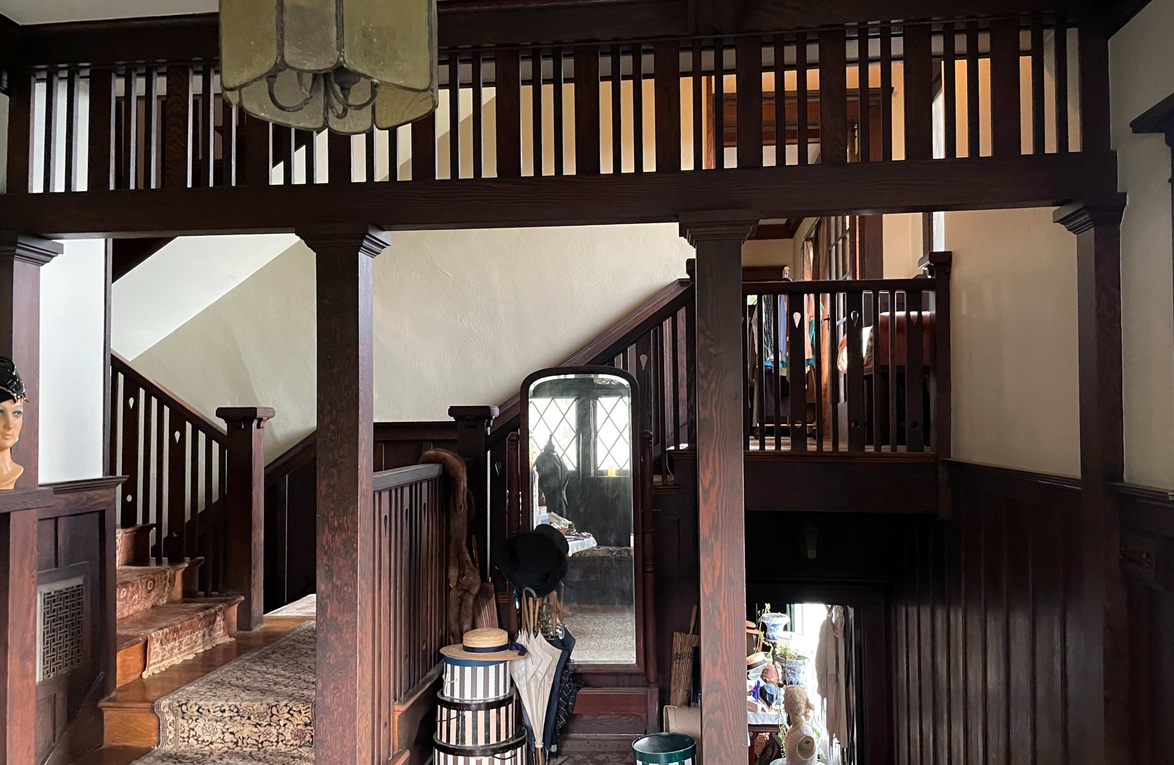 A wooden staircase in a vintage-style home, with a mirror reflecting a hallway and various items placed on the floor.