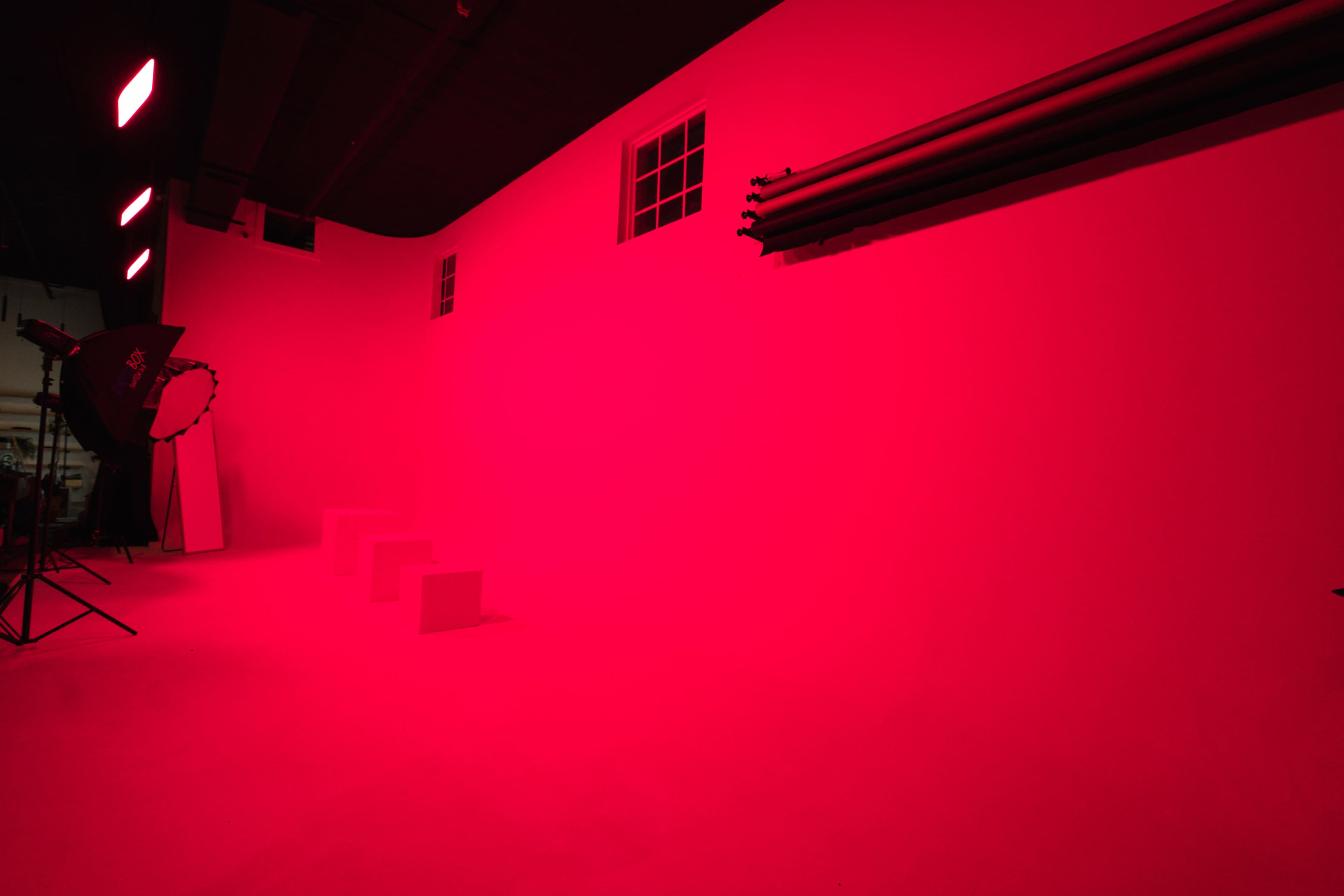 A studio space with a brightly lit red backdrop, featuring three white steps and some lighting equipment.