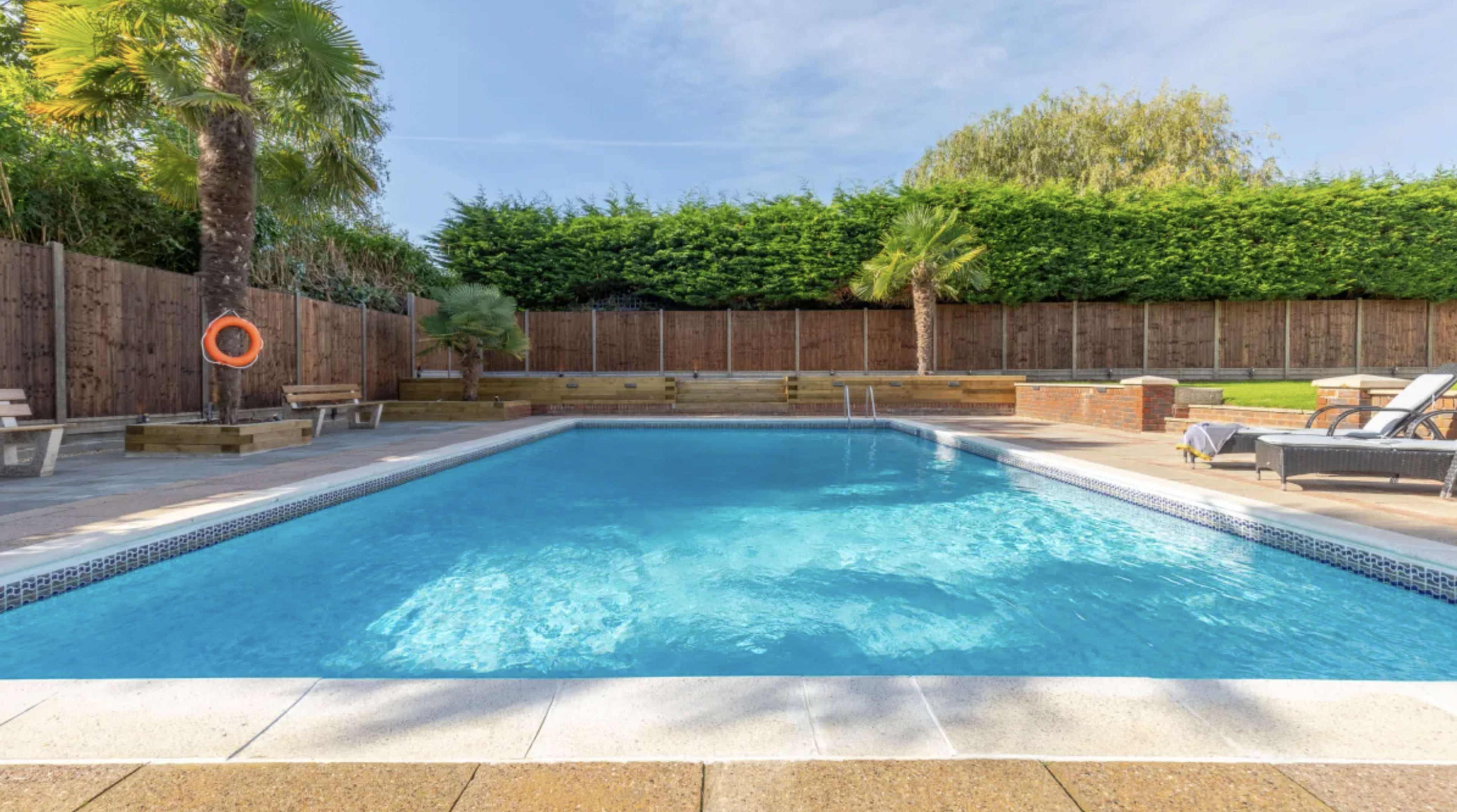 A clear swimming pool surrounded by palm trees and wooden seating areas.