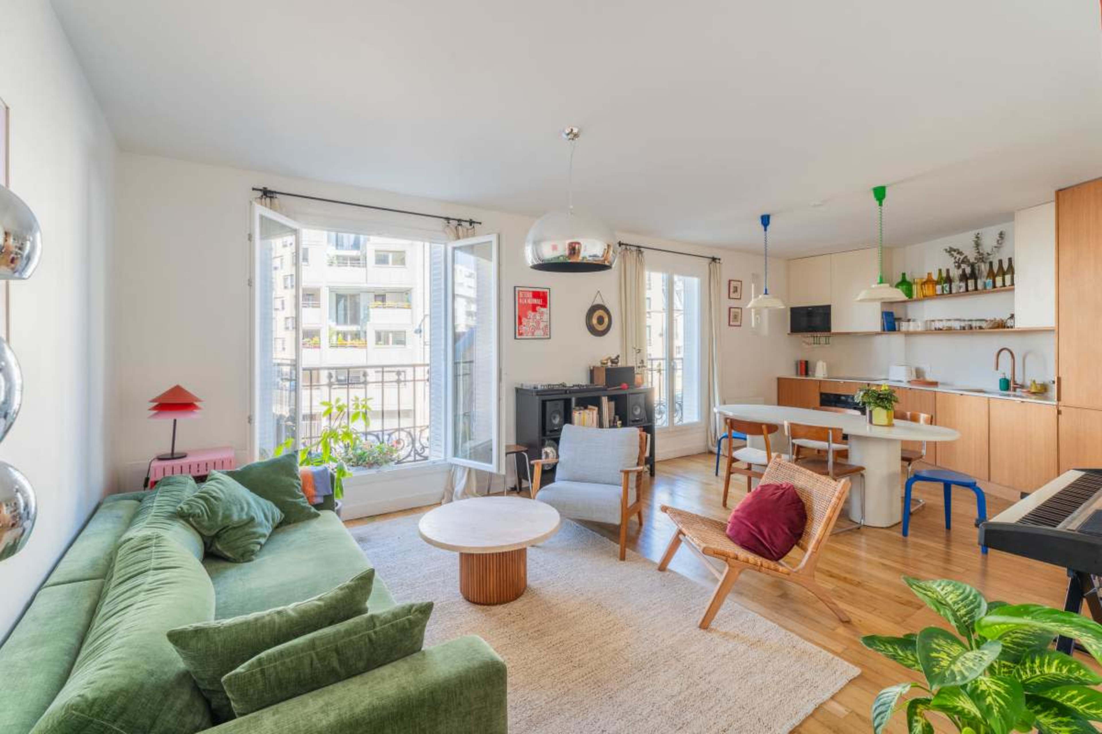 A modern living room features a green sofa, a round wooden coffee table, and a combination of light and wooden furnishings, with large windows letting in natural light.