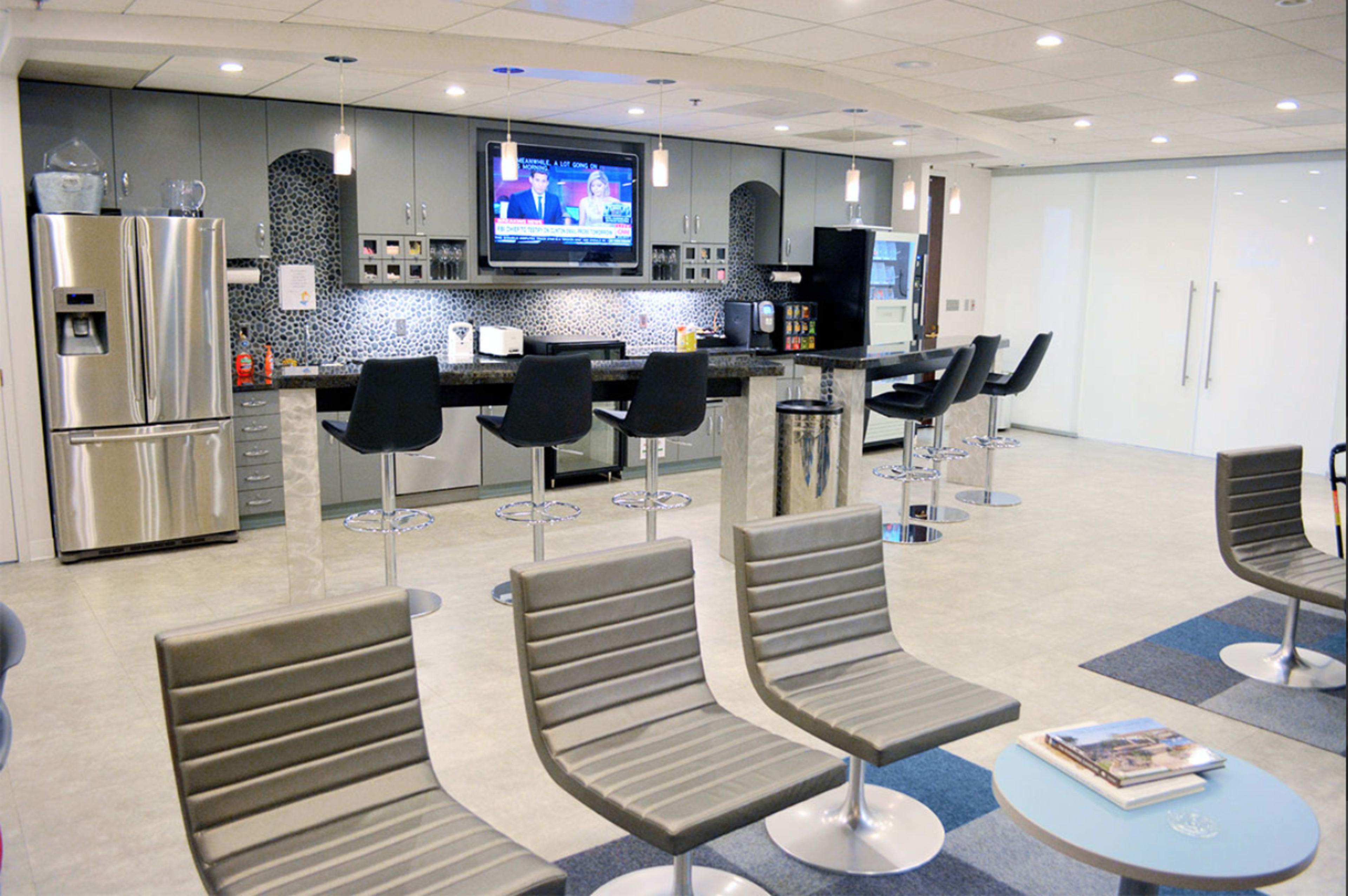A modern kitchen and lounge area with bar stools, stainless steel appliances, and a television mounted on the wall.