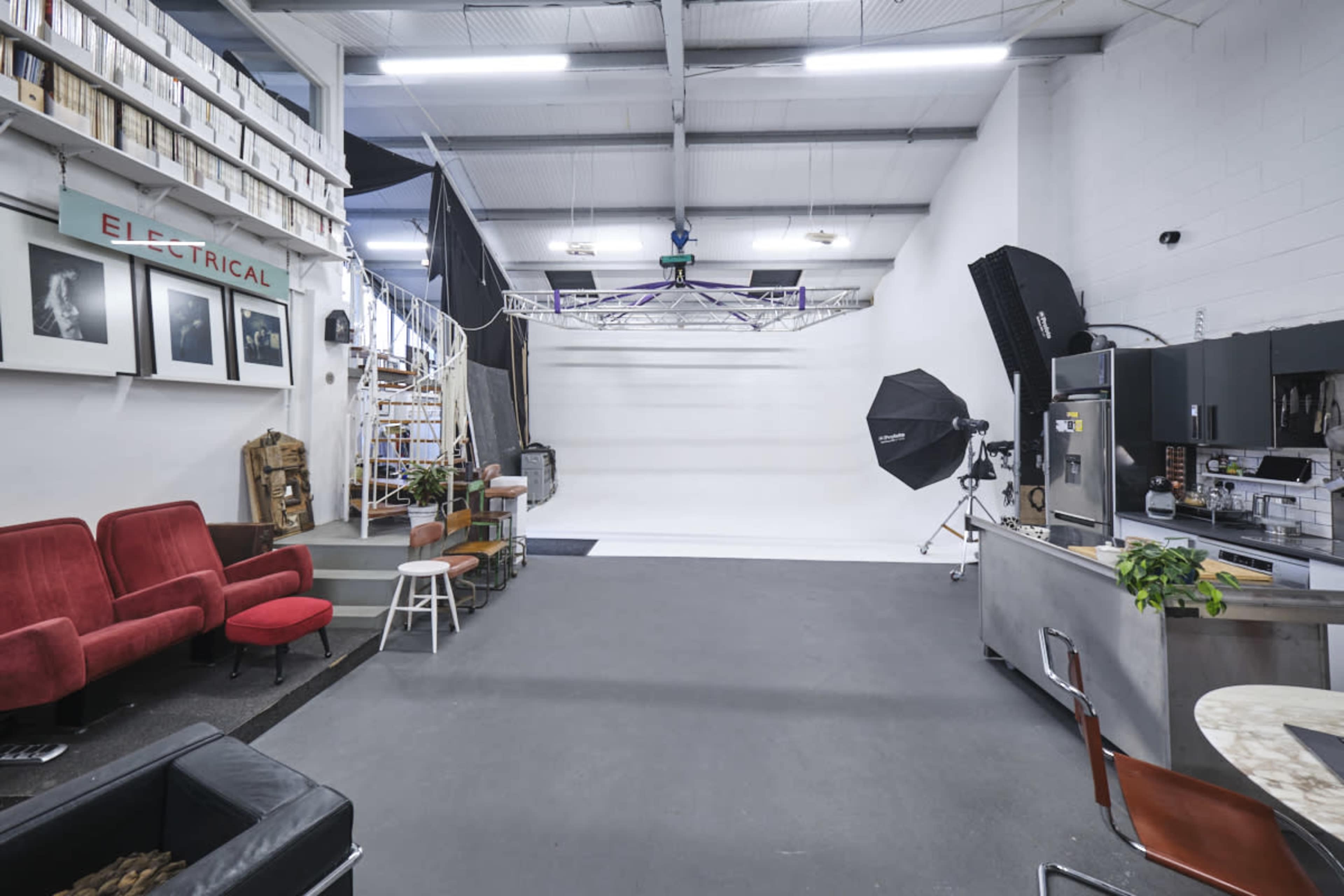 A spacious photography studio with a white backdrop, seating areas, and a kitchenette.