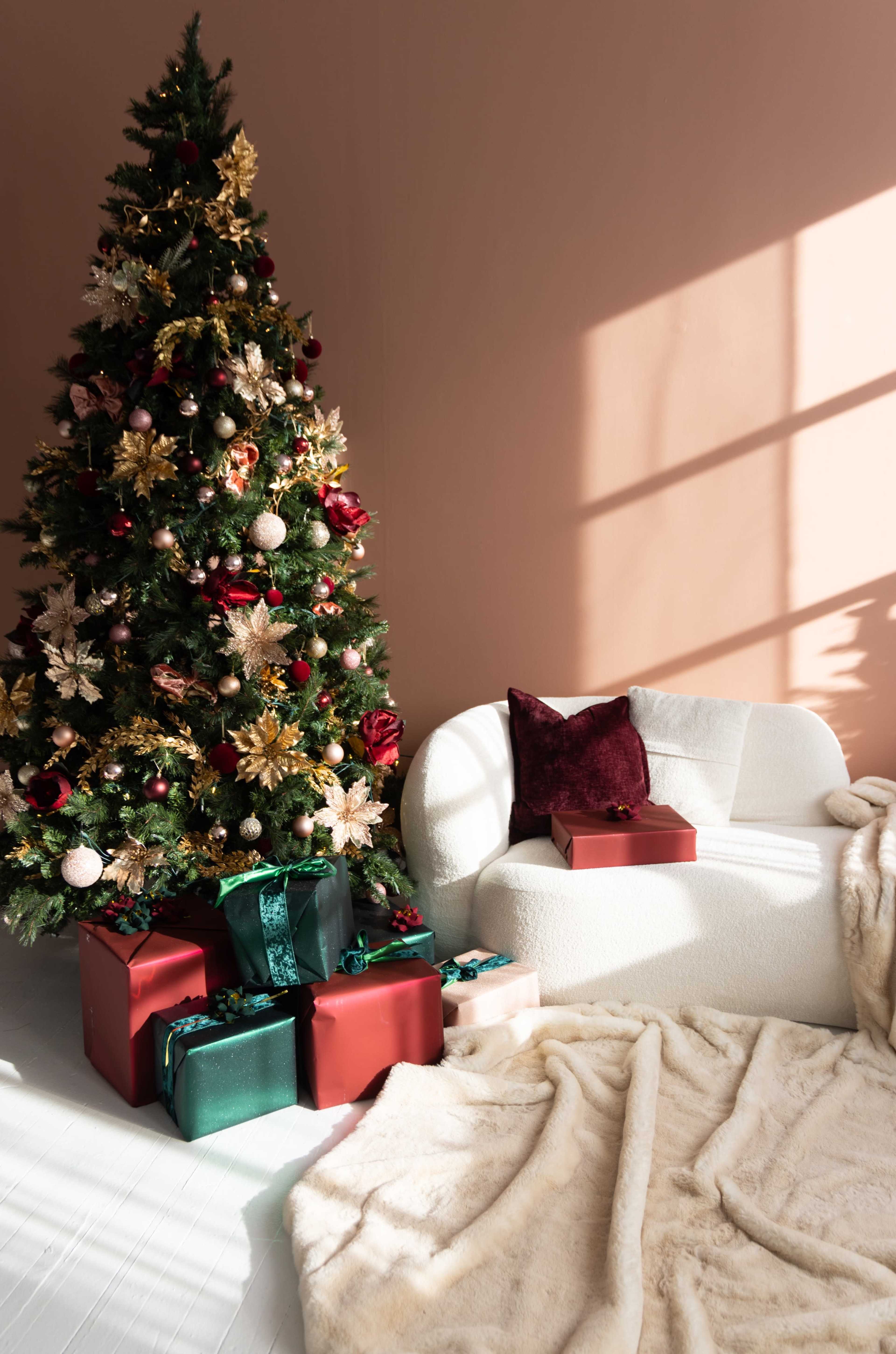 A decorated Christmas tree stands beside a white sofa adorned with a cozy blanket and an assortment of wrapped gifts underneath.