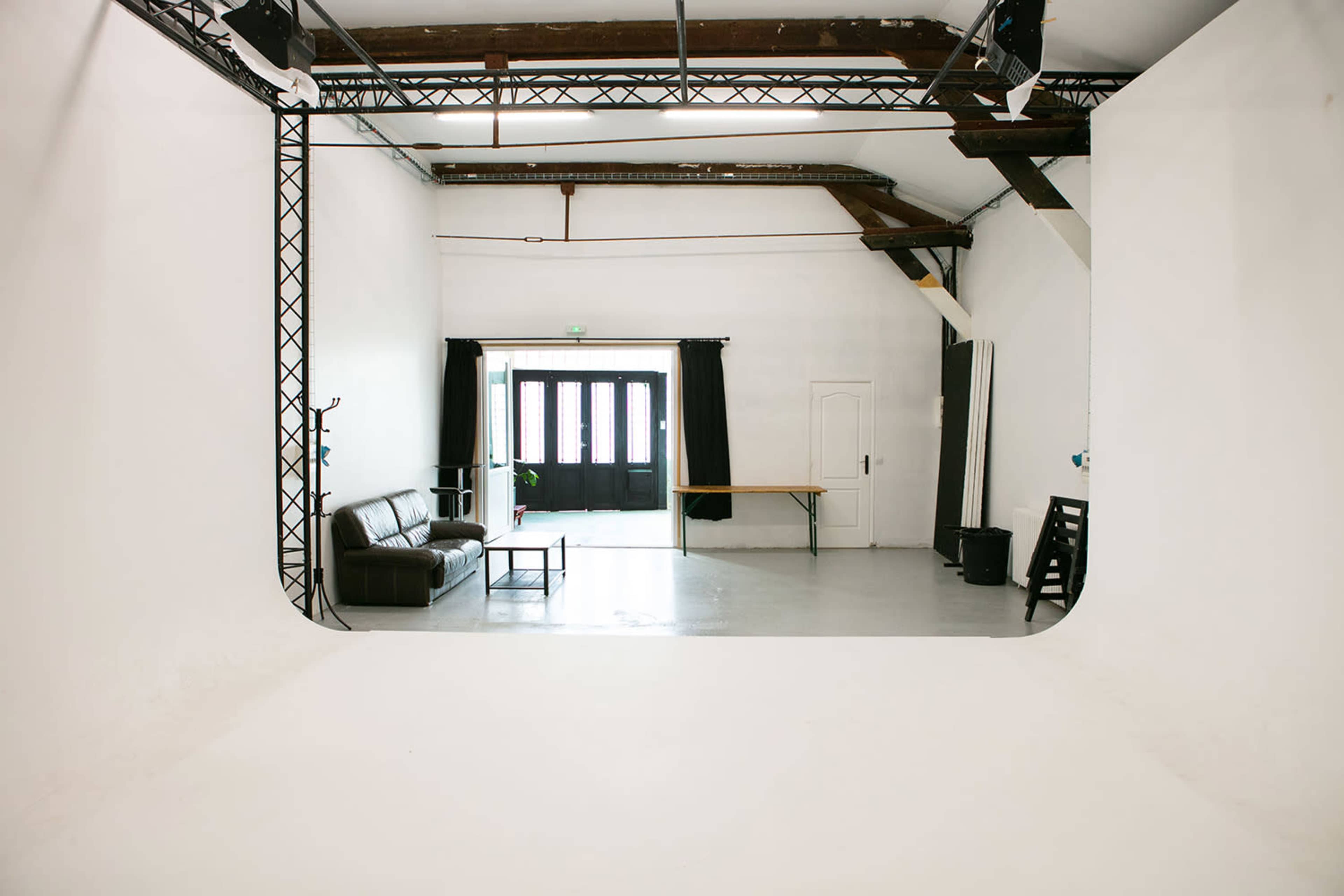 A spacious, minimalist studio with a leather sofa, a wooden table, and large windows framed by black curtains.