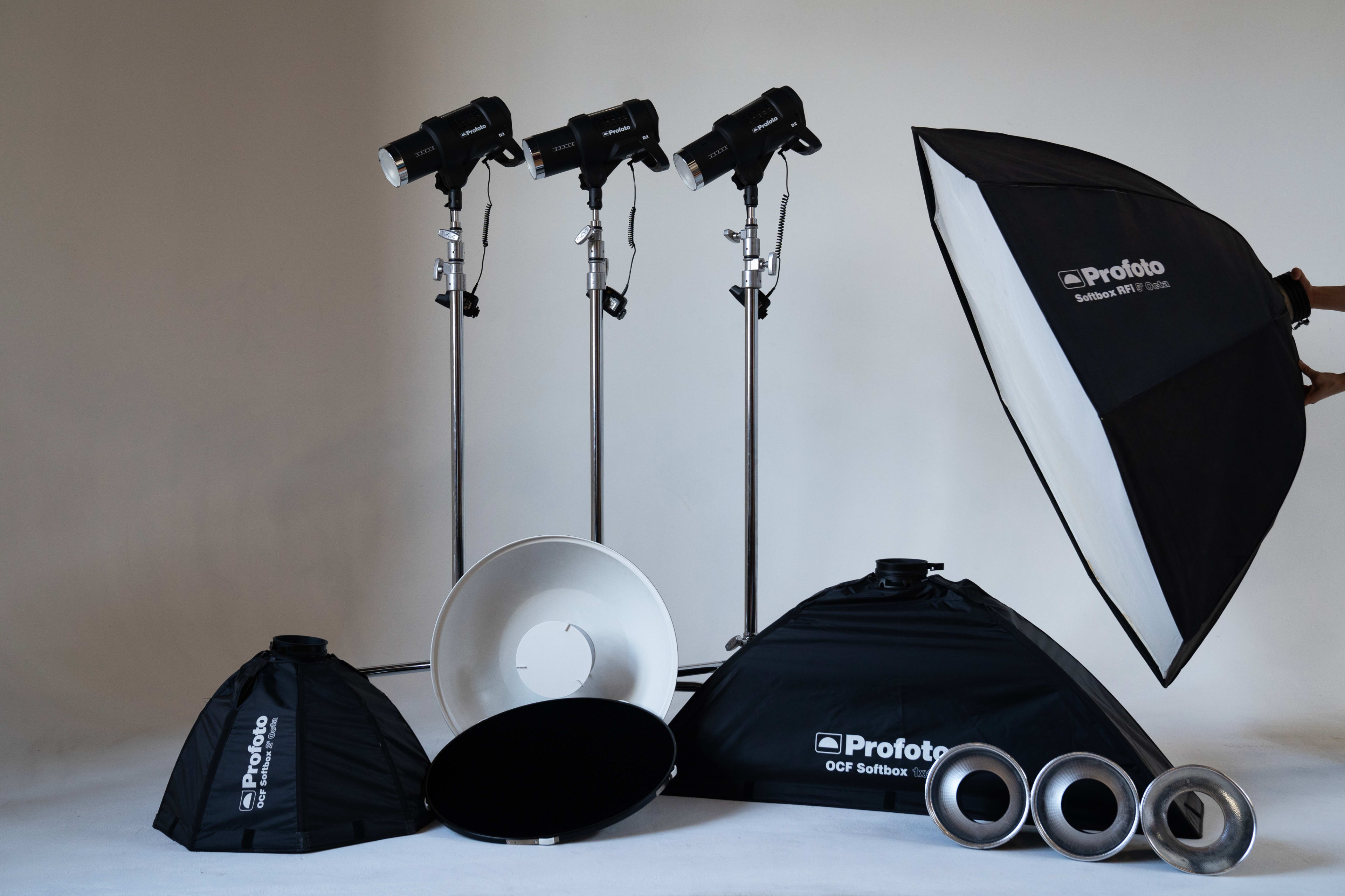 The image shows a variety of photography lighting equipment, including three light stands with softboxes, a reflector, and several other lighting accessories arranged against a neutral background.