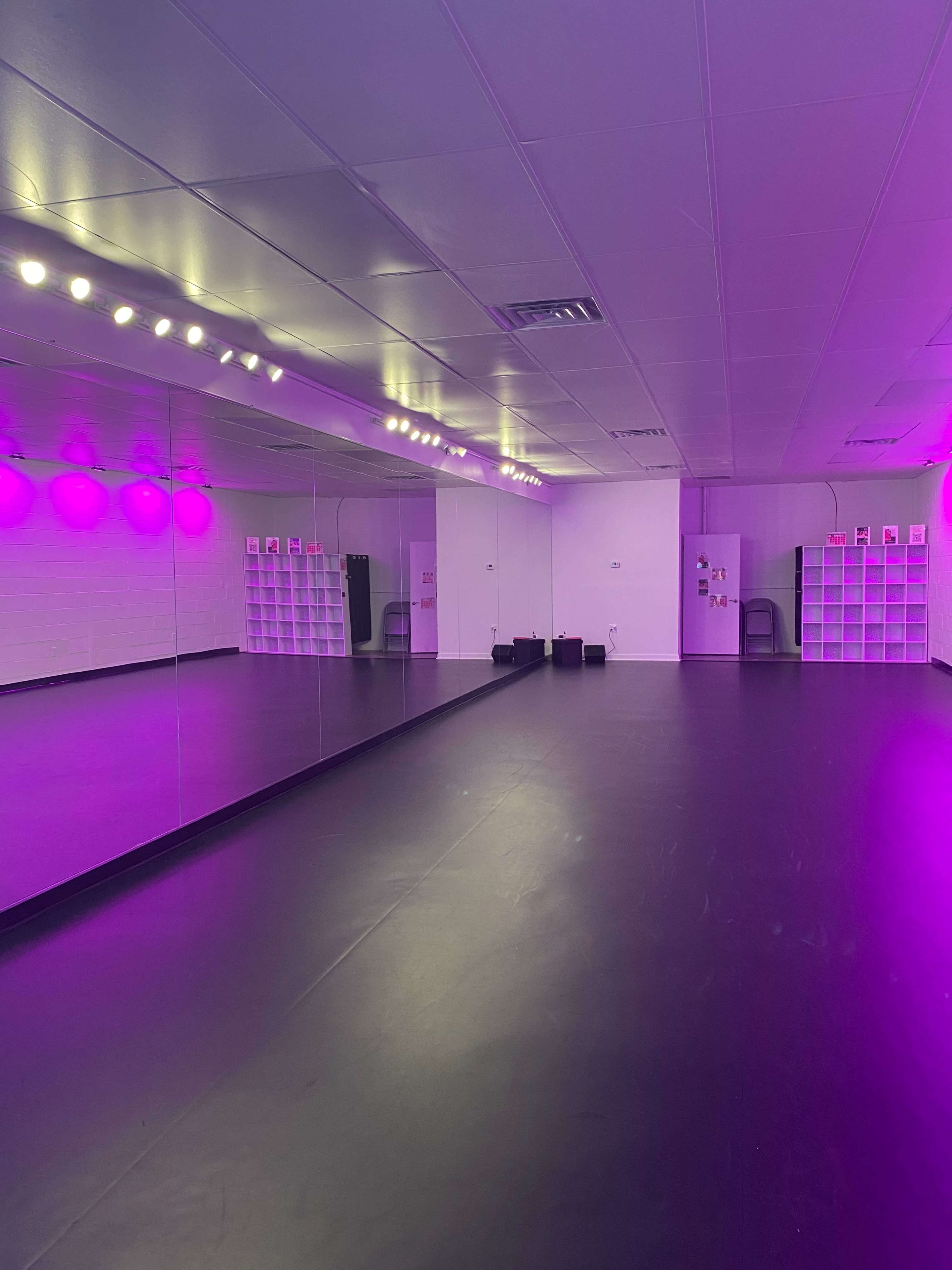 A spacious dance studio with purple lighting, mirrored walls, and black flooring.