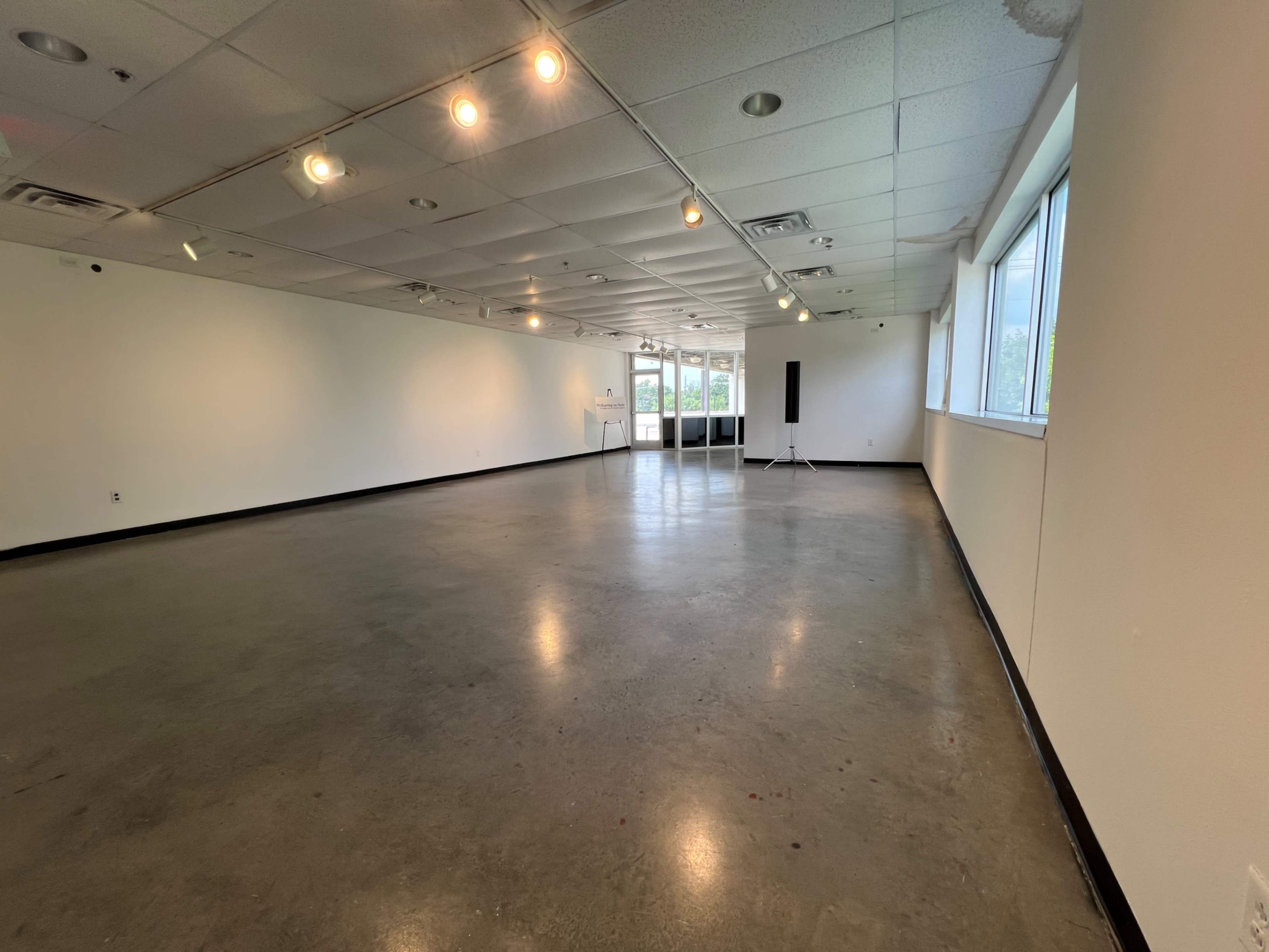 The image shows a spacious, empty gallery with polished concrete flooring and overhead lighting.