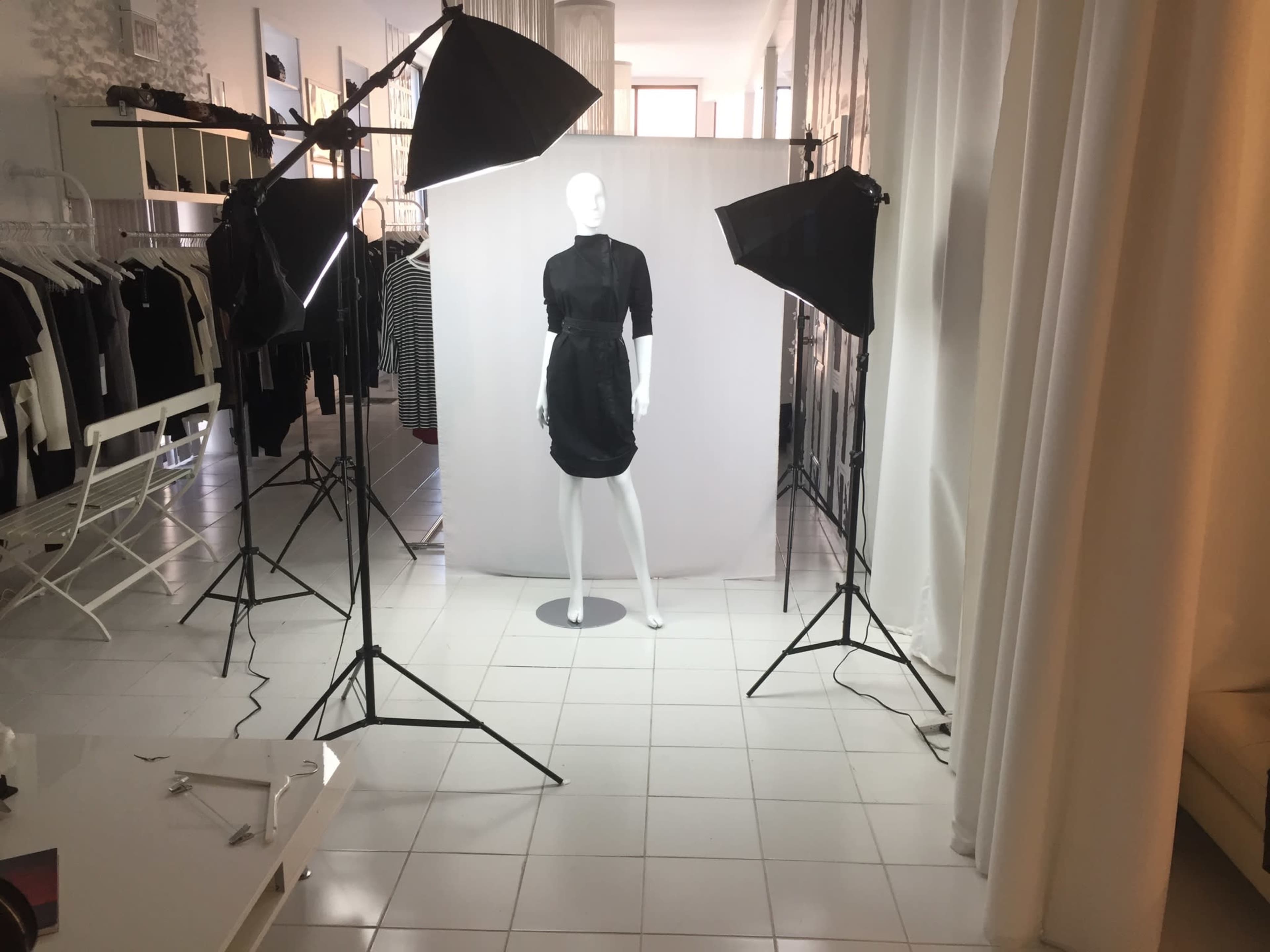 A mannequin is positioned under soft lighting in a studio setting, surrounded by clothing displays and a neutral backdrop.