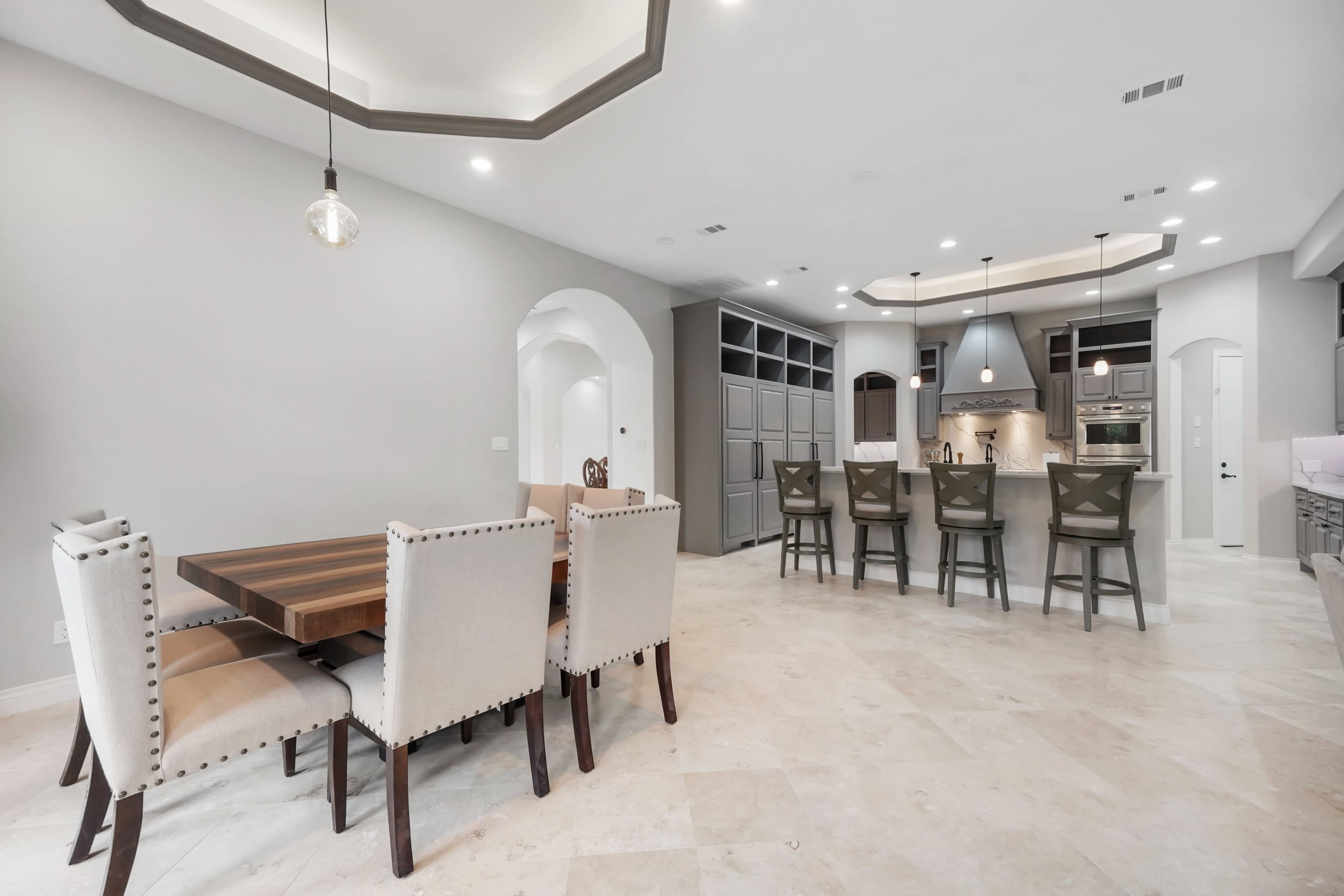 A modern kitchen and dining area featuring a wooden dining table with upholstered chairs and a kitchen island with bar stools.