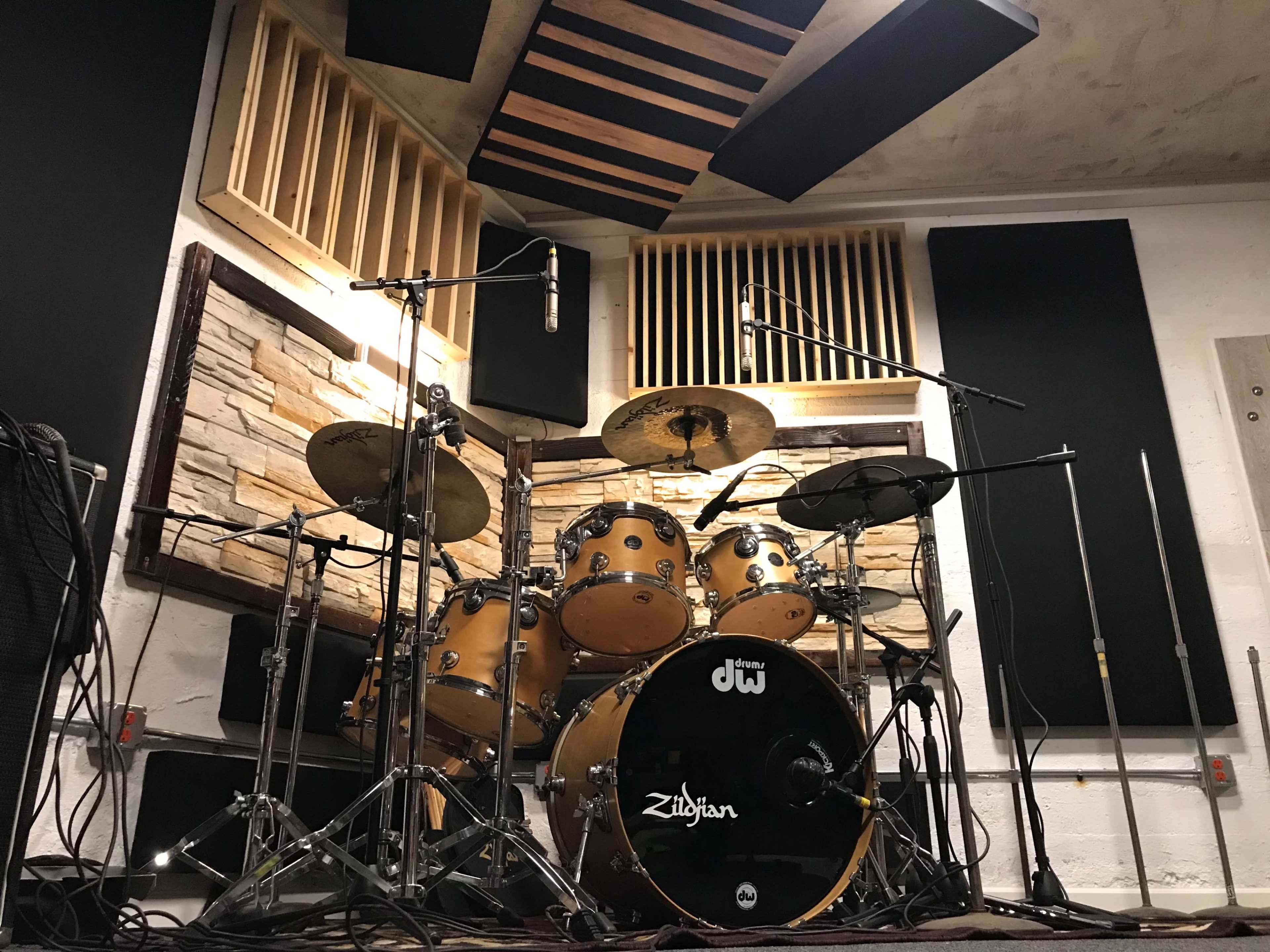 The image shows a professional drum set arranged in a soundproof recording studio, with wooden panels and acoustic treatment on the walls.