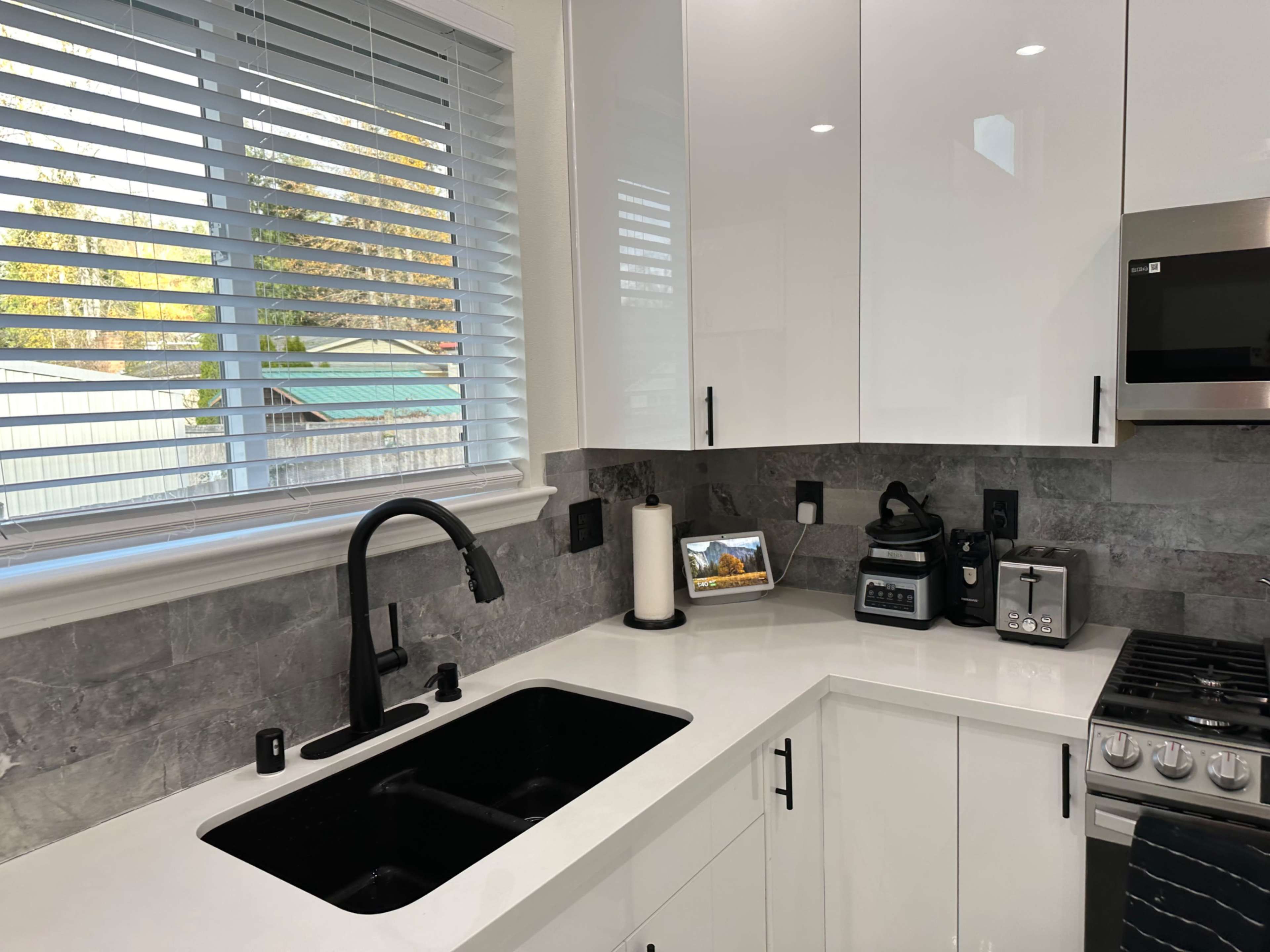 A modern kitchen with a black sink, gray stone backsplash, and stainless steel appliances, including a gas stove and a coffee maker.