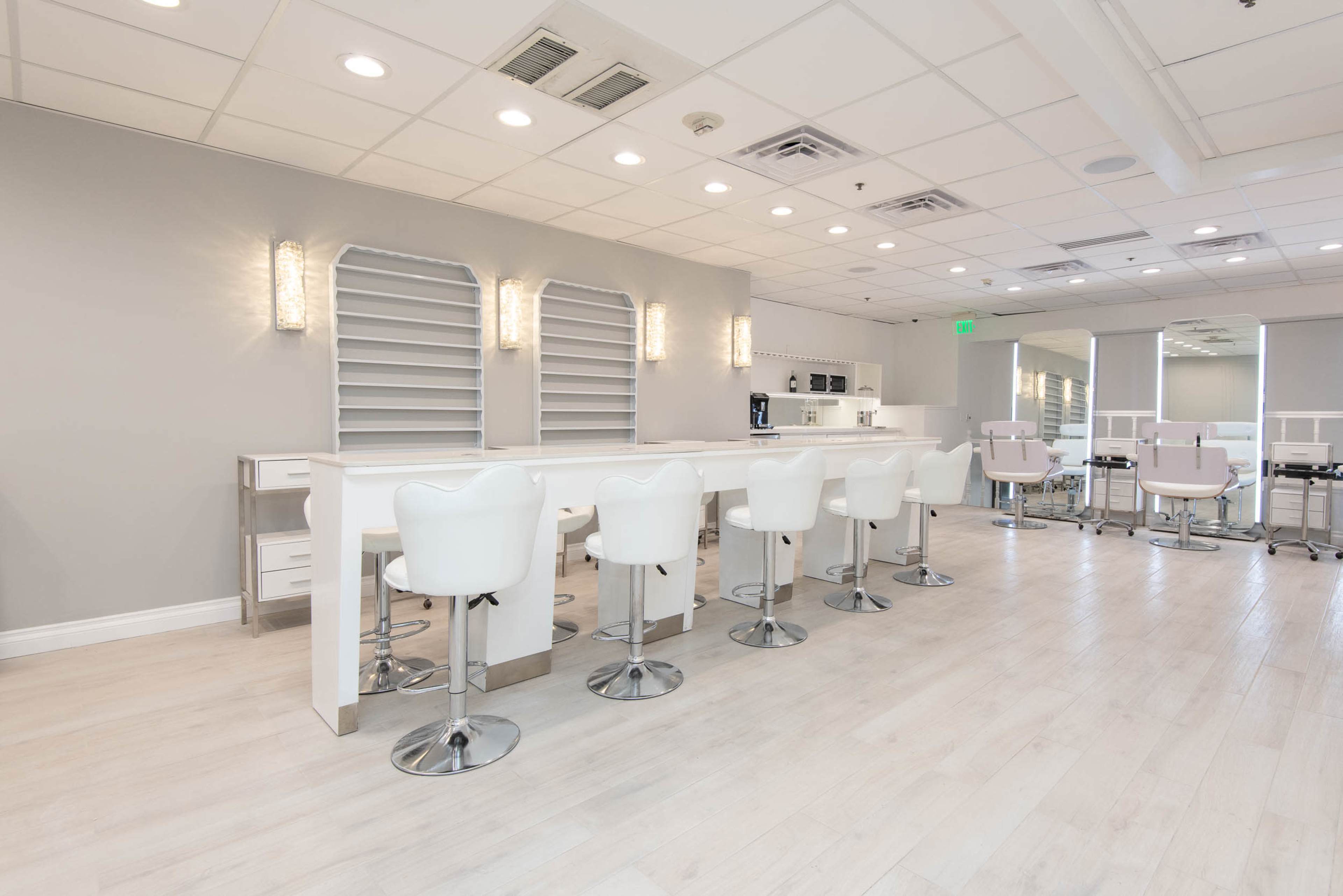 The image shows a modern, minimalist bar area with white stools and a counter in a well-lit room.