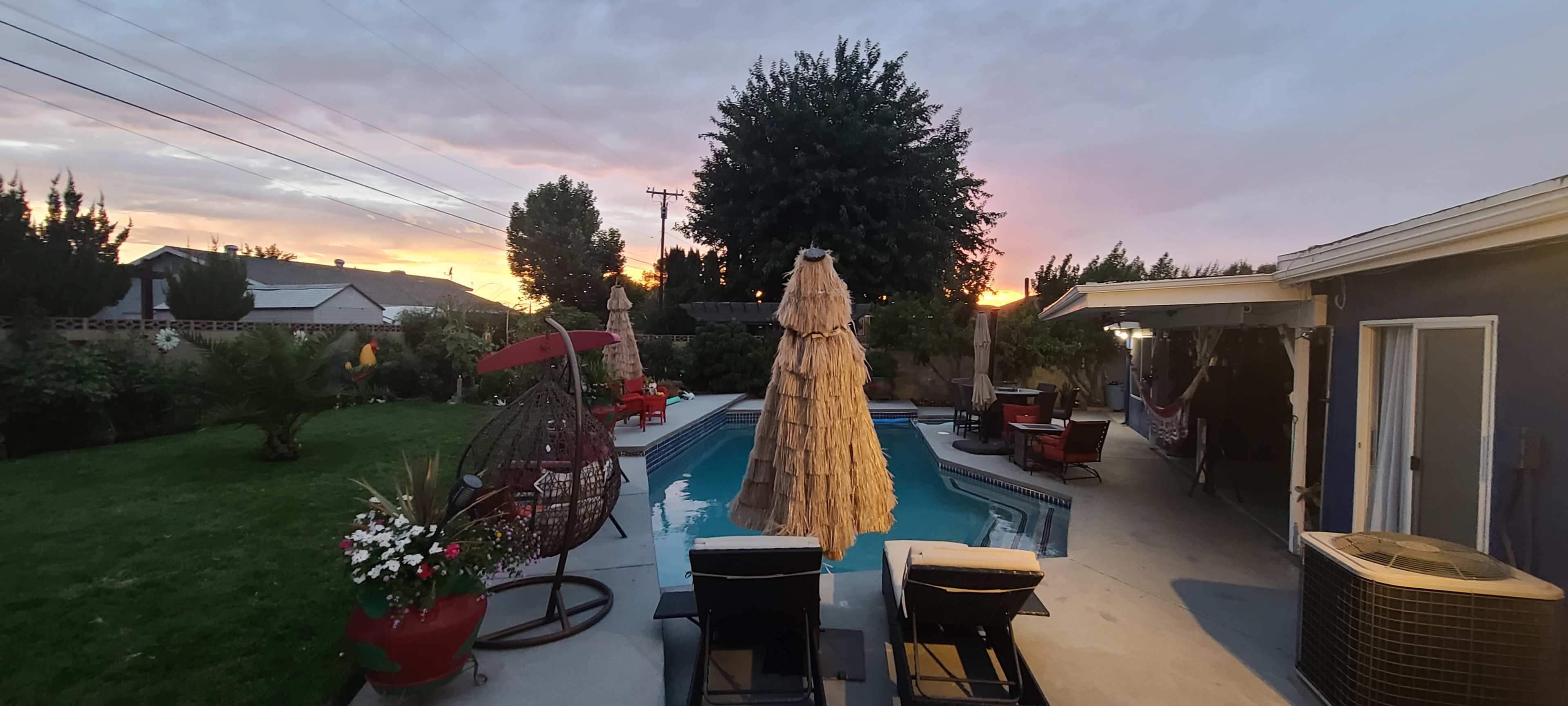 A backyard with a swimming pool, patio furniture, and a hammock under a sunset sky.