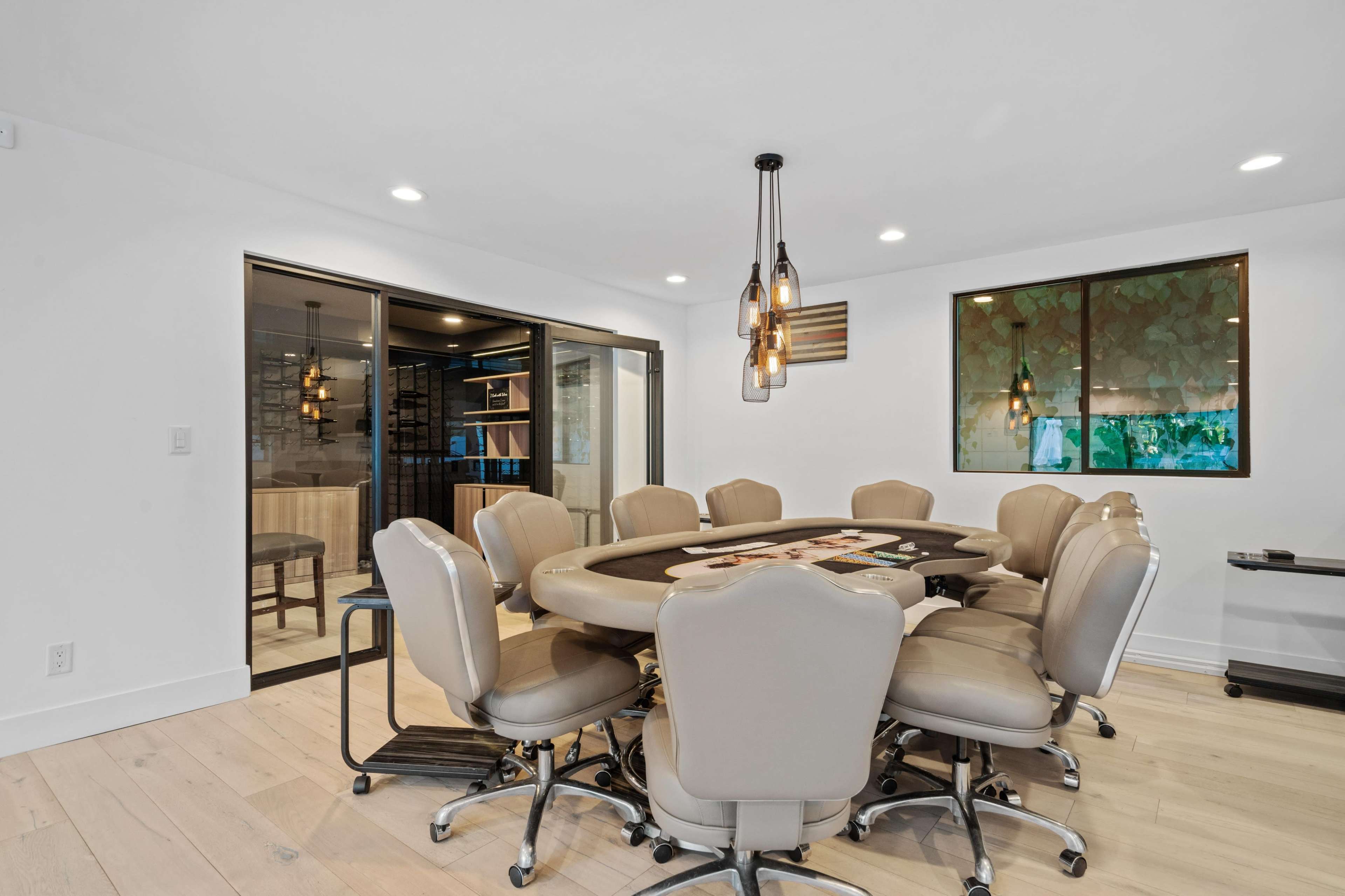 A modern, well-lit poker room with a large round table surrounded by twelve beige chairs, adjacent to a glass-walled space.
