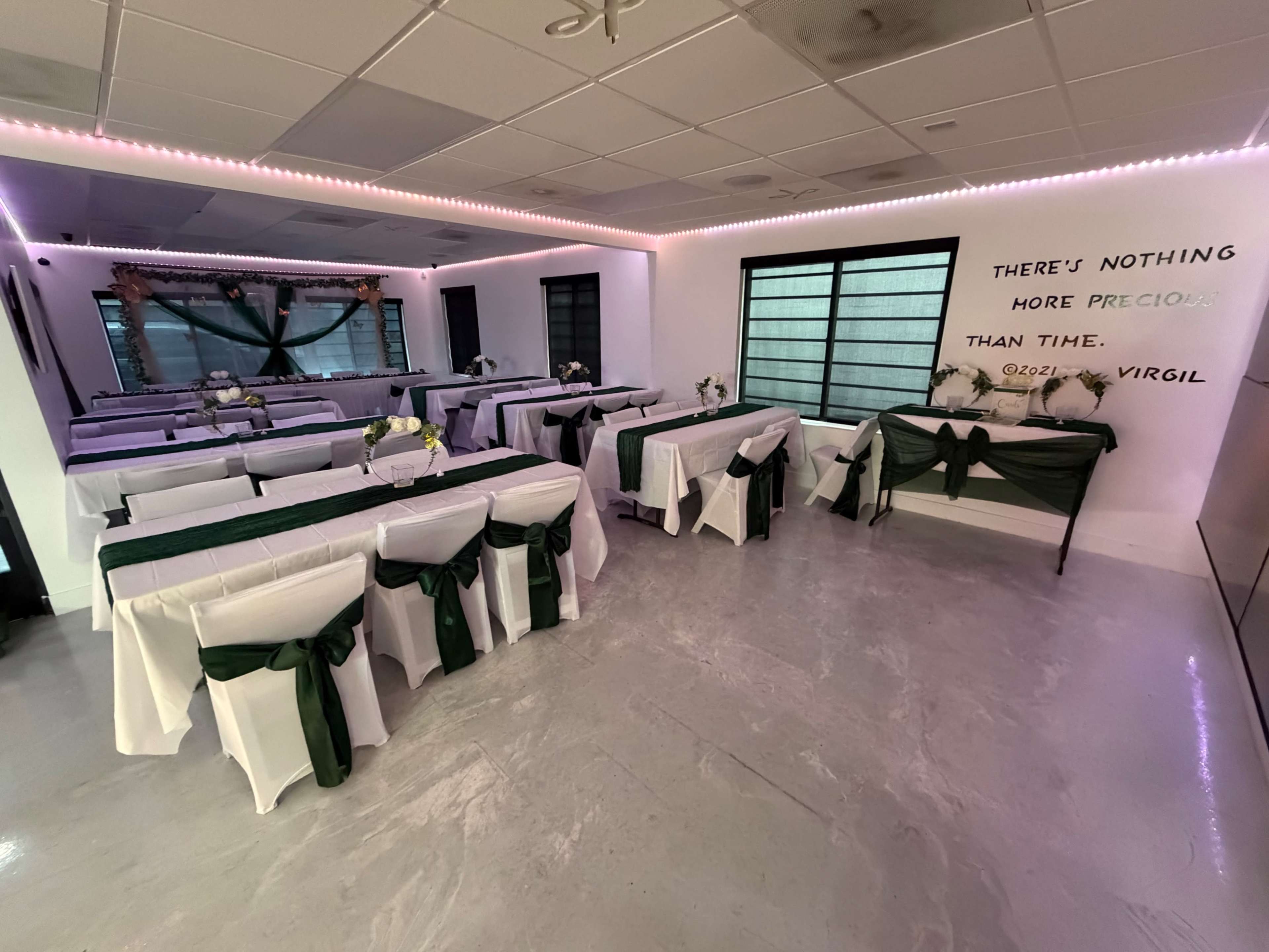 The image shows a decorated indoor venue with multiple tables covered in white tablecloths and green sashes, arranged for a gathering.