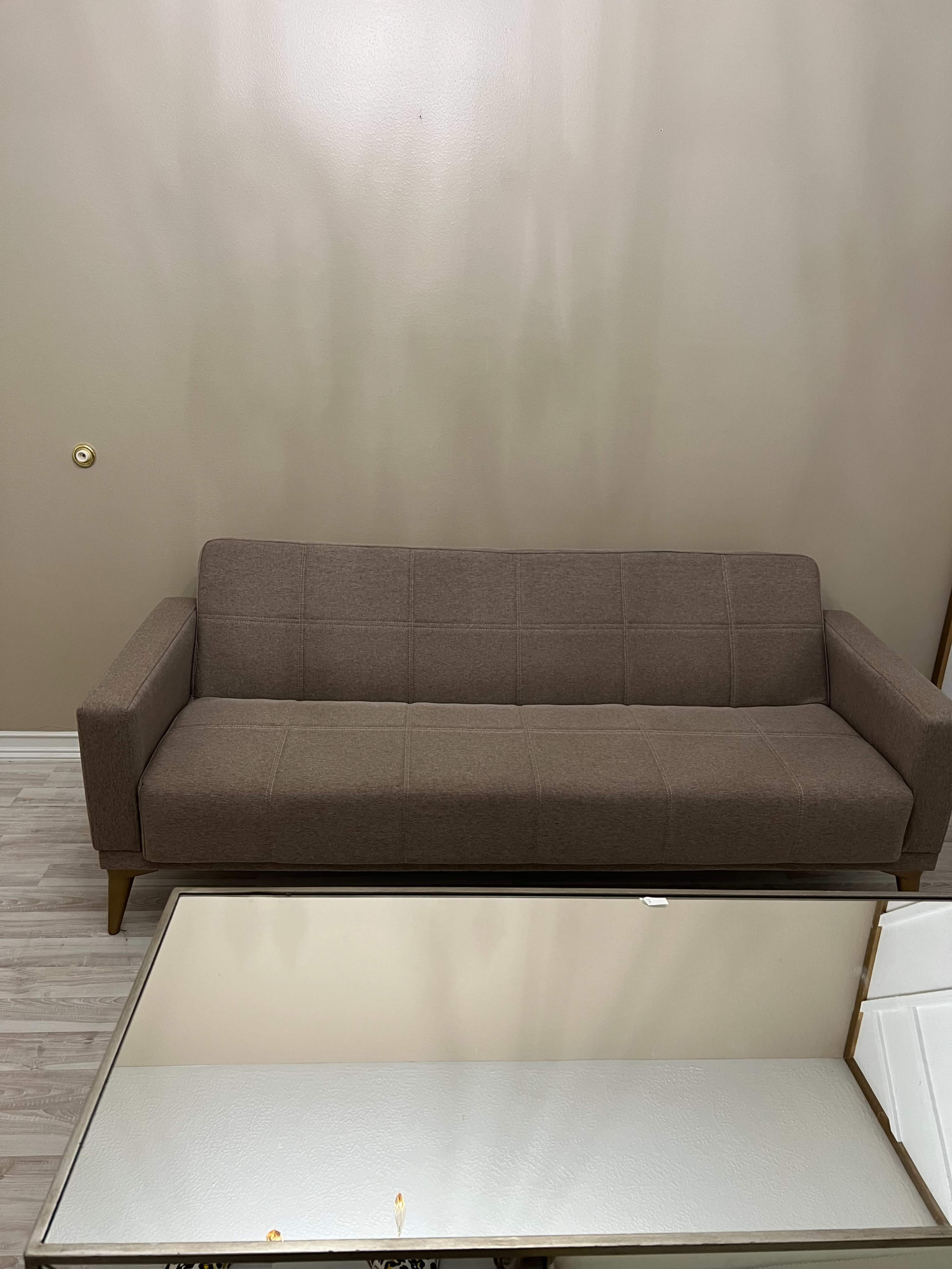 A brown sofa with a grid pattern is positioned against a plain wall, and a reflective coffee table is in the foreground.