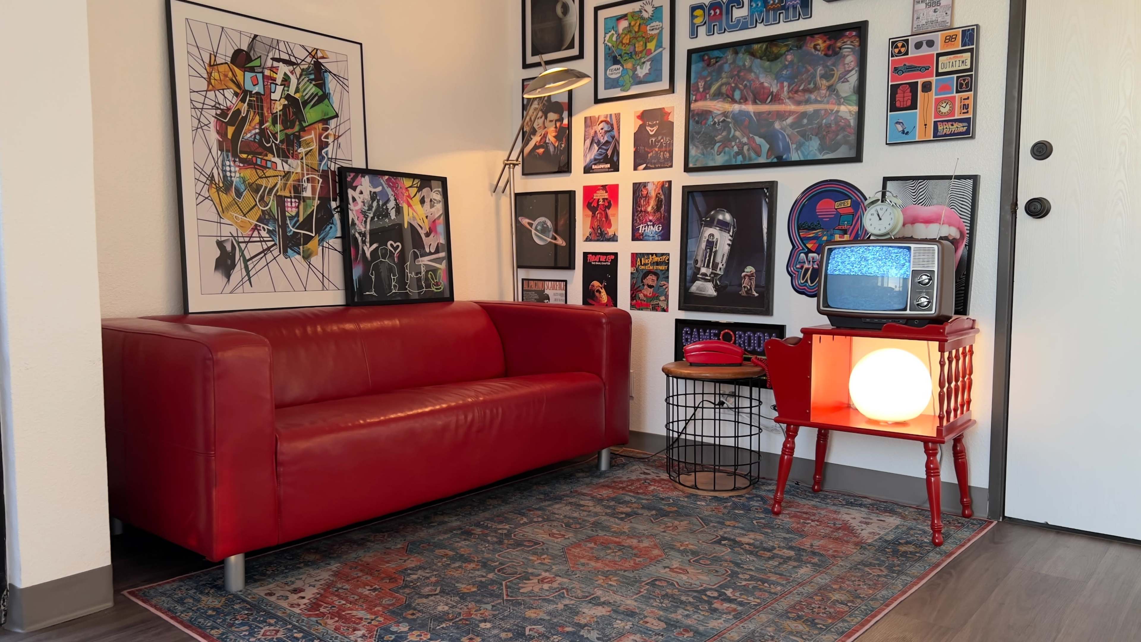 The scene features a red sofa positioned in a room adorned with various framed artworks and retro decor, including a vintage television and a round lamp on a side table.