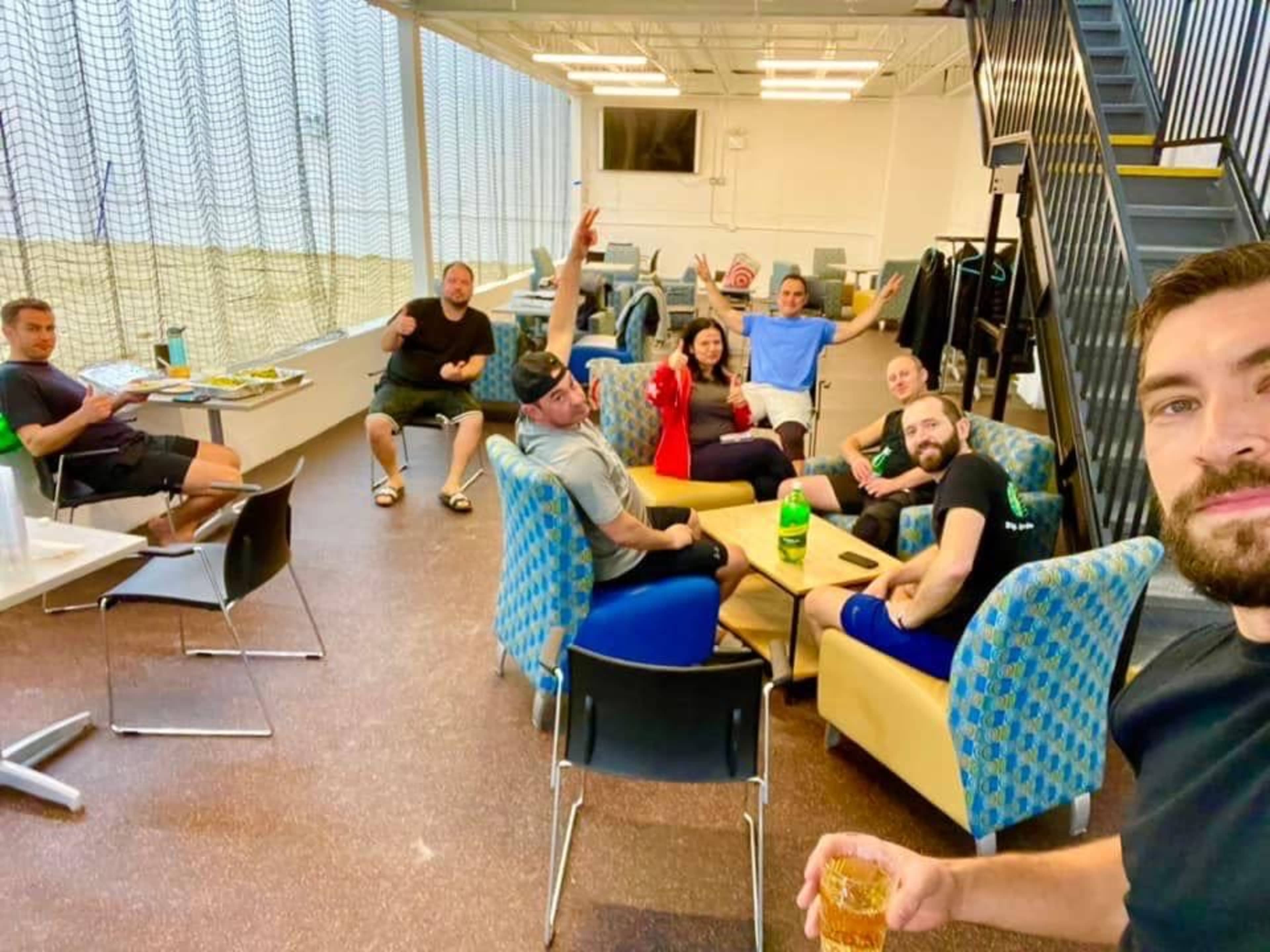 A group of people is gathered in a lounge area, sitting and standing in various poses while engaging with one another.