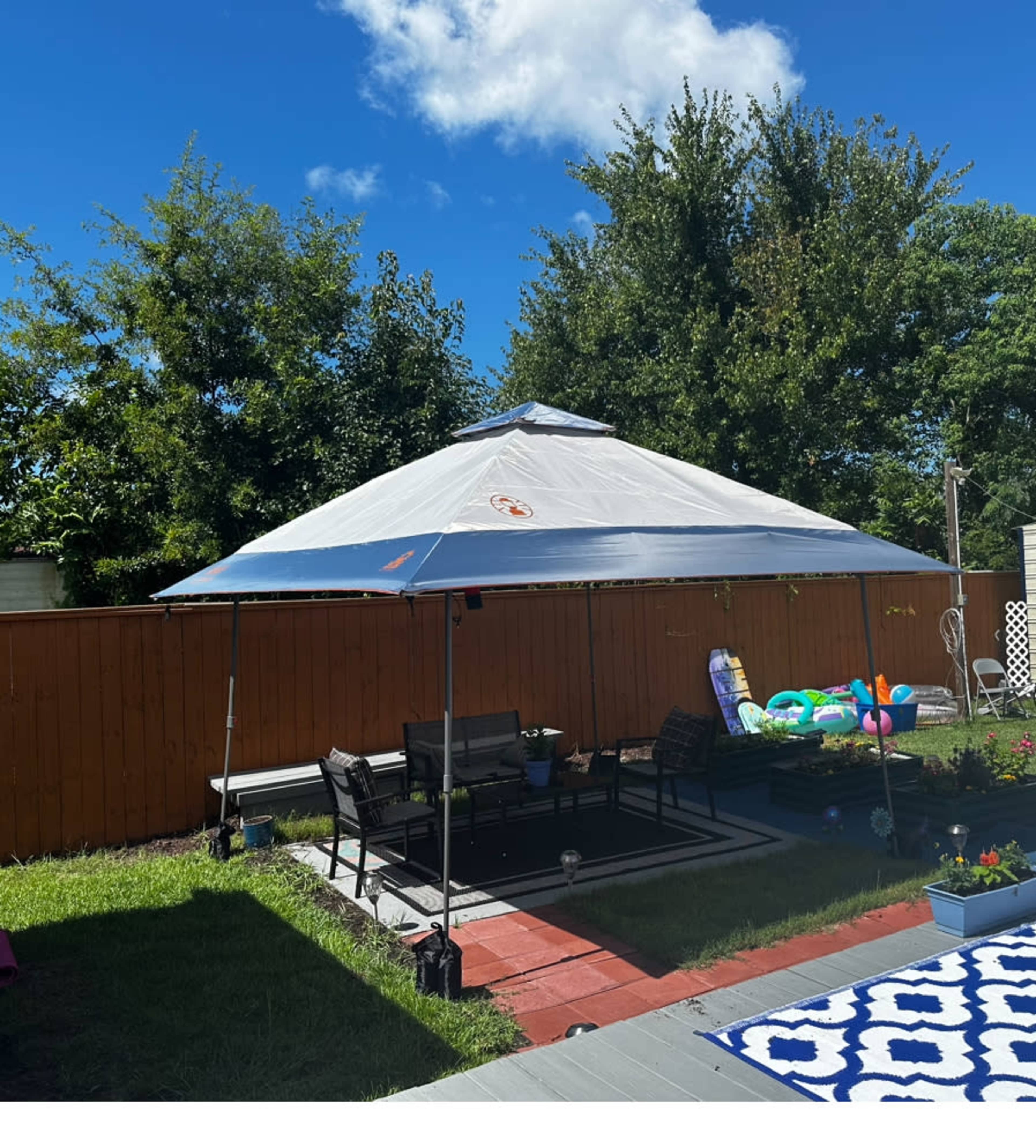 A large, square canopy stands over a patio area filled with seating and surrounded by greenery.