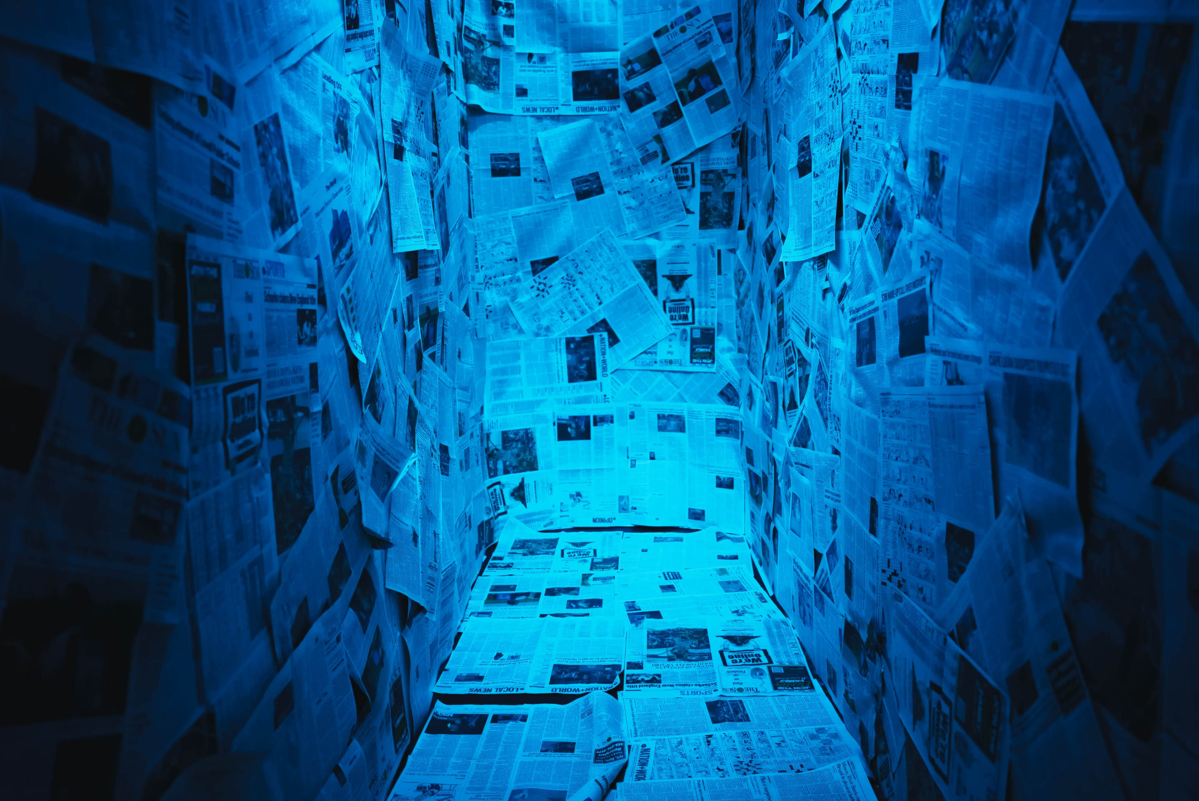 The scene features a narrow corridor lined with blue-tinged newspapers covering the walls and floor.