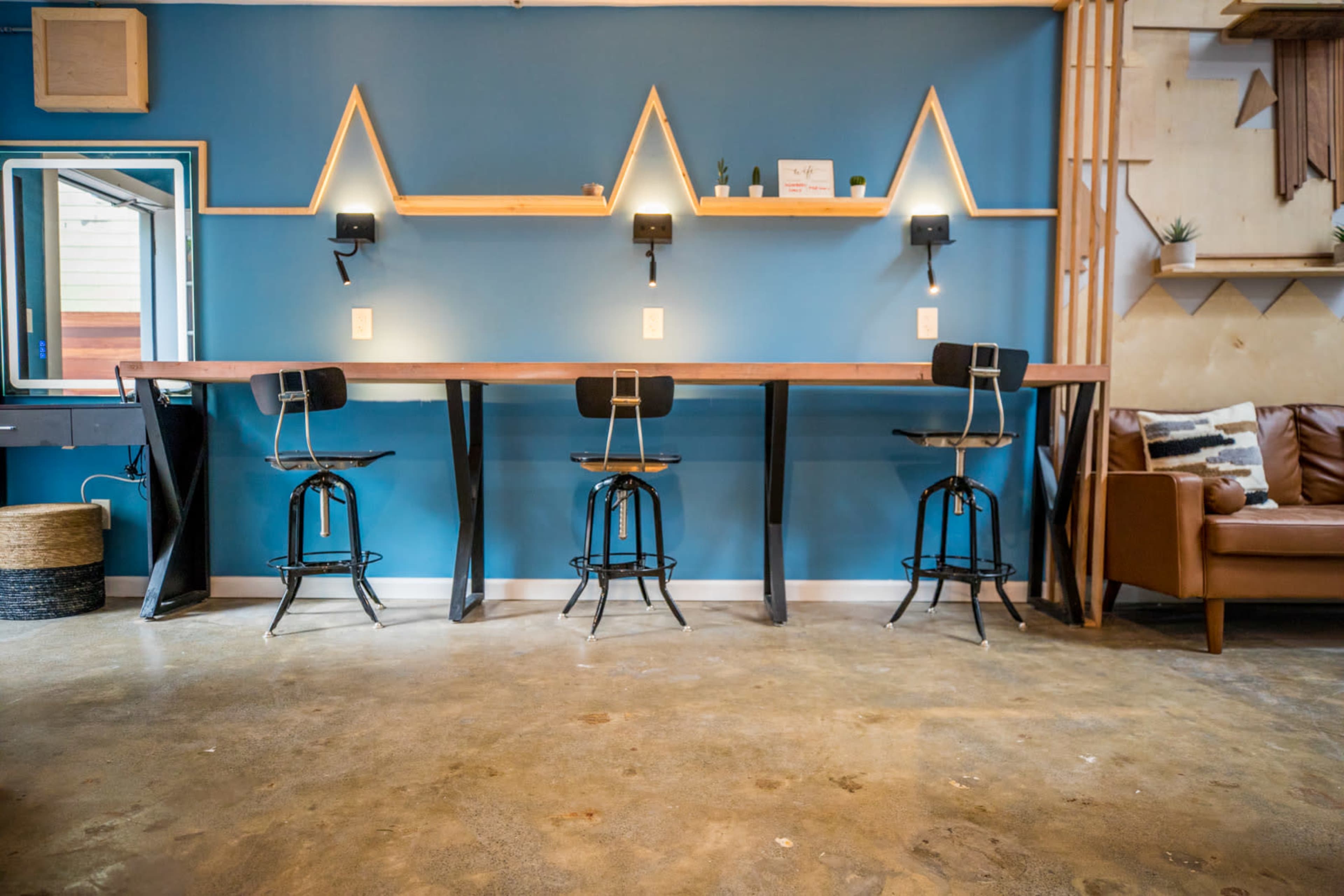 The image shows a modern interior with a high table and four stools against a blue wall, featuring shelves with minimalistic decor above.