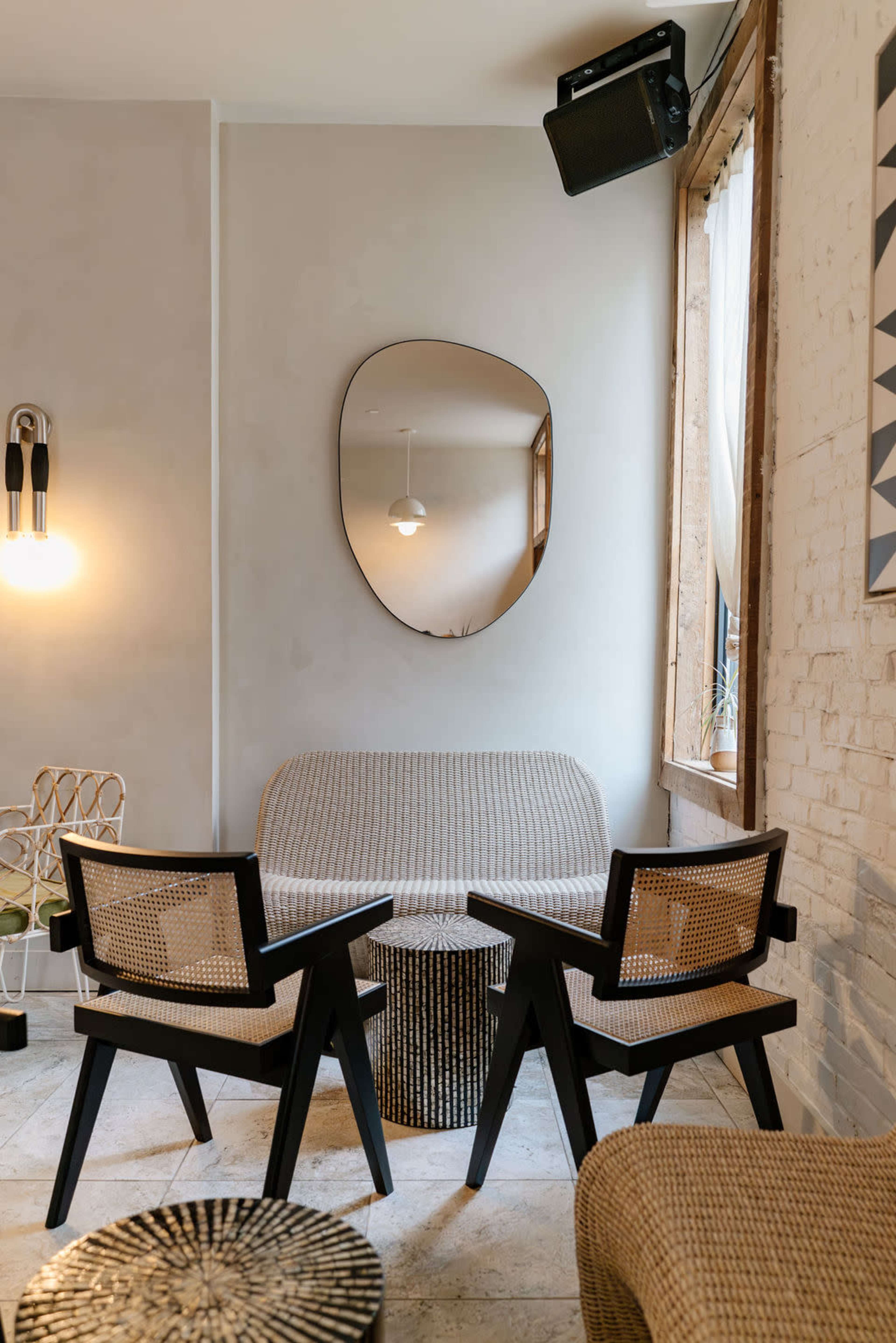 The image shows a cozy seating area with two black chairs and a textured sofa, complemented by a round coffee table and an oval mirror on the wall.