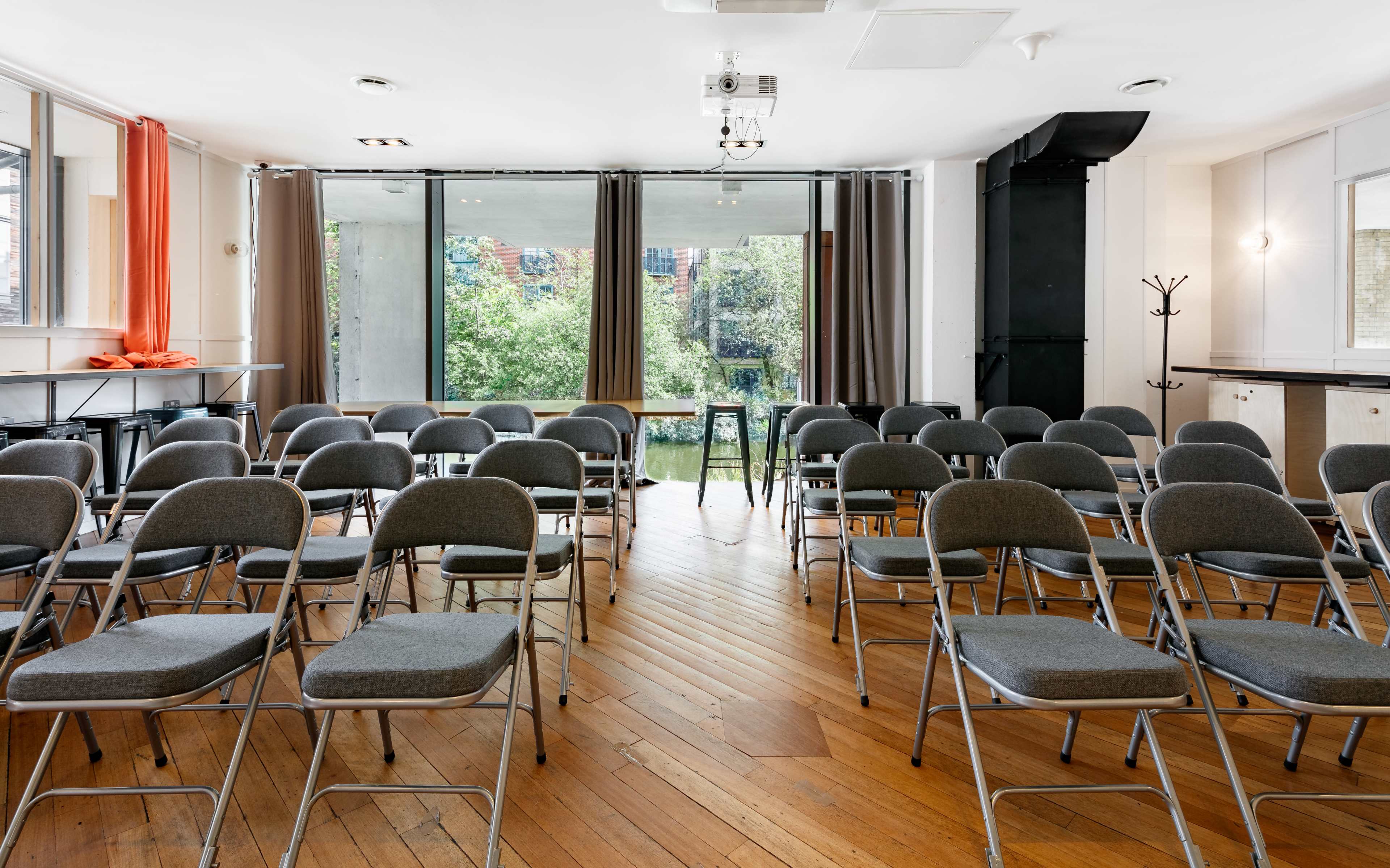 A meeting room with rows of gray folding chairs arranged in front of a large window overlooking greenery.