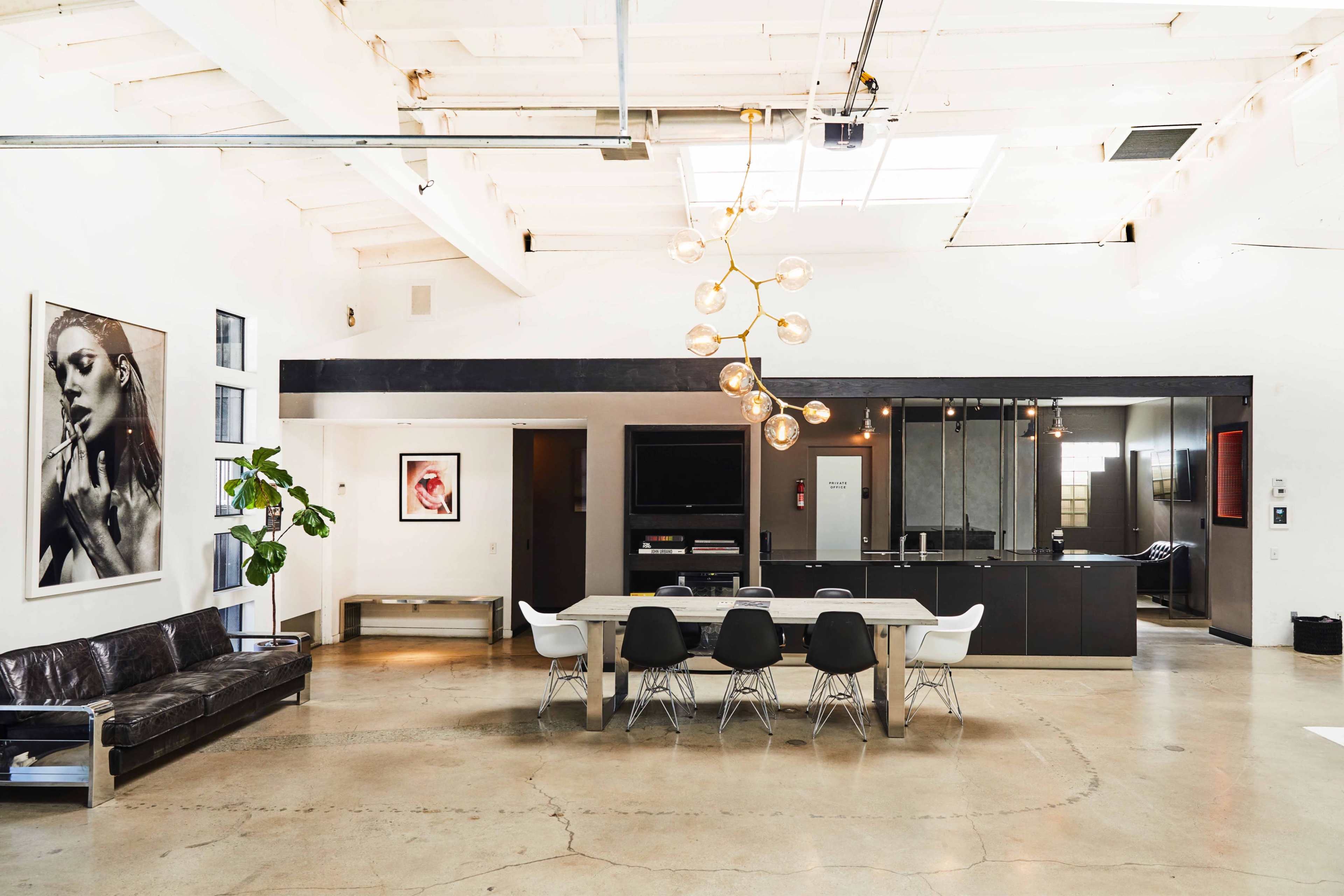 A modern, open-concept living space featuring a leather sofa, a dining table surrounded by chairs, and a kitchen area with sleek cabinetry.