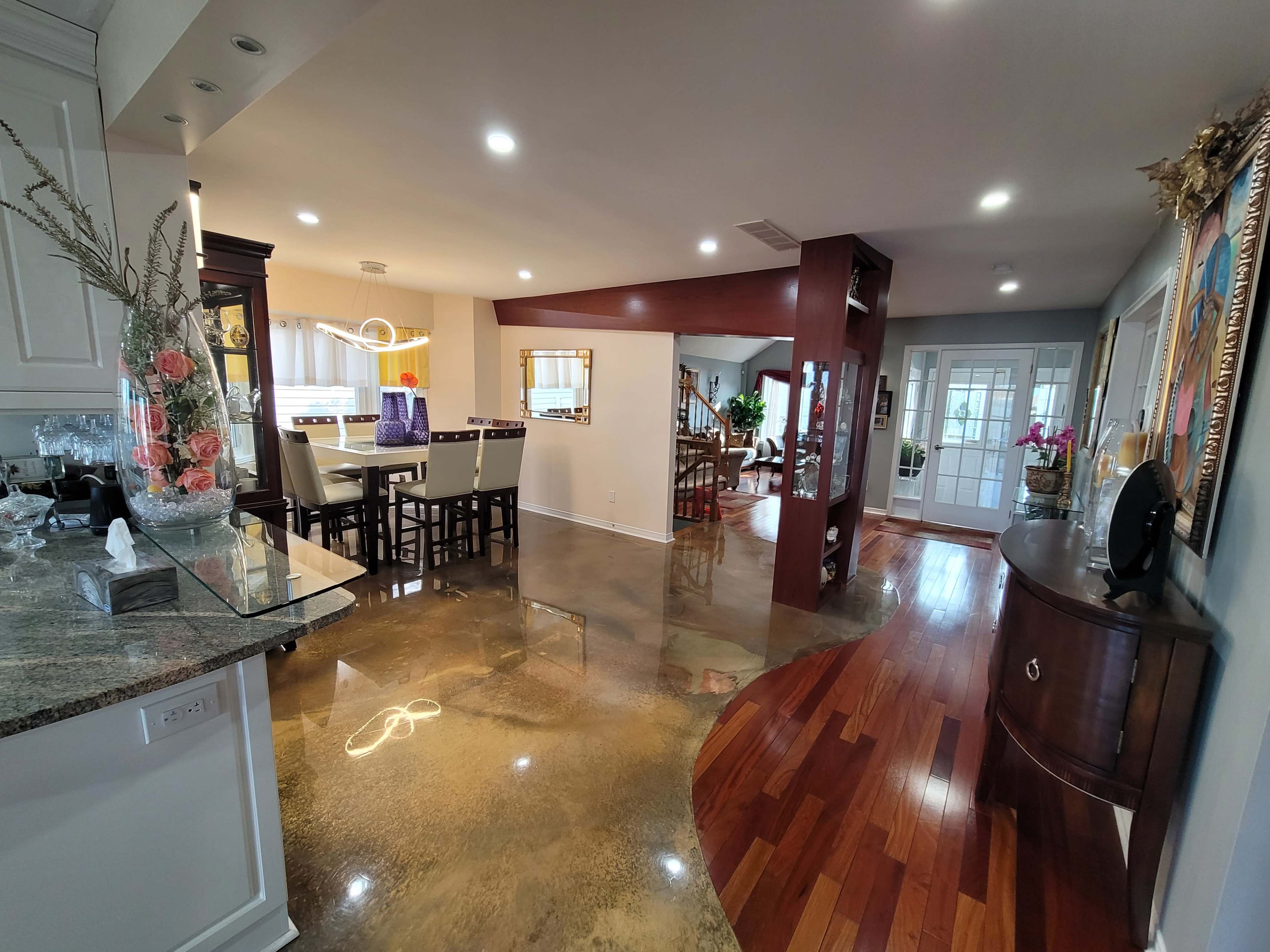 A modern open-concept living space featuring a kitchen with a breakfast bar, a dining area, and a hallway leading to a staircase.